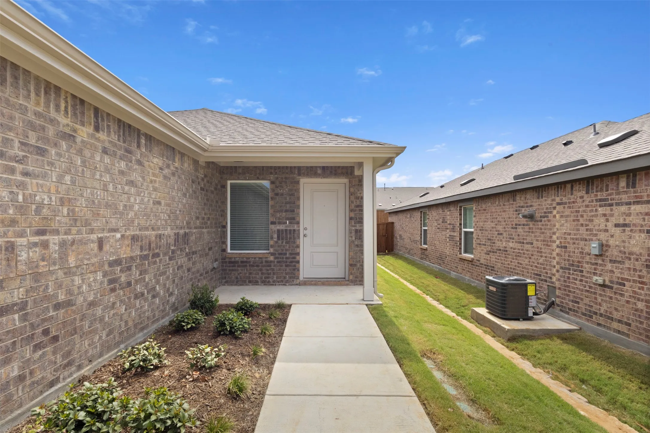 Brick exterior with a covered entry, concrete walkway, and landscaped planting beds