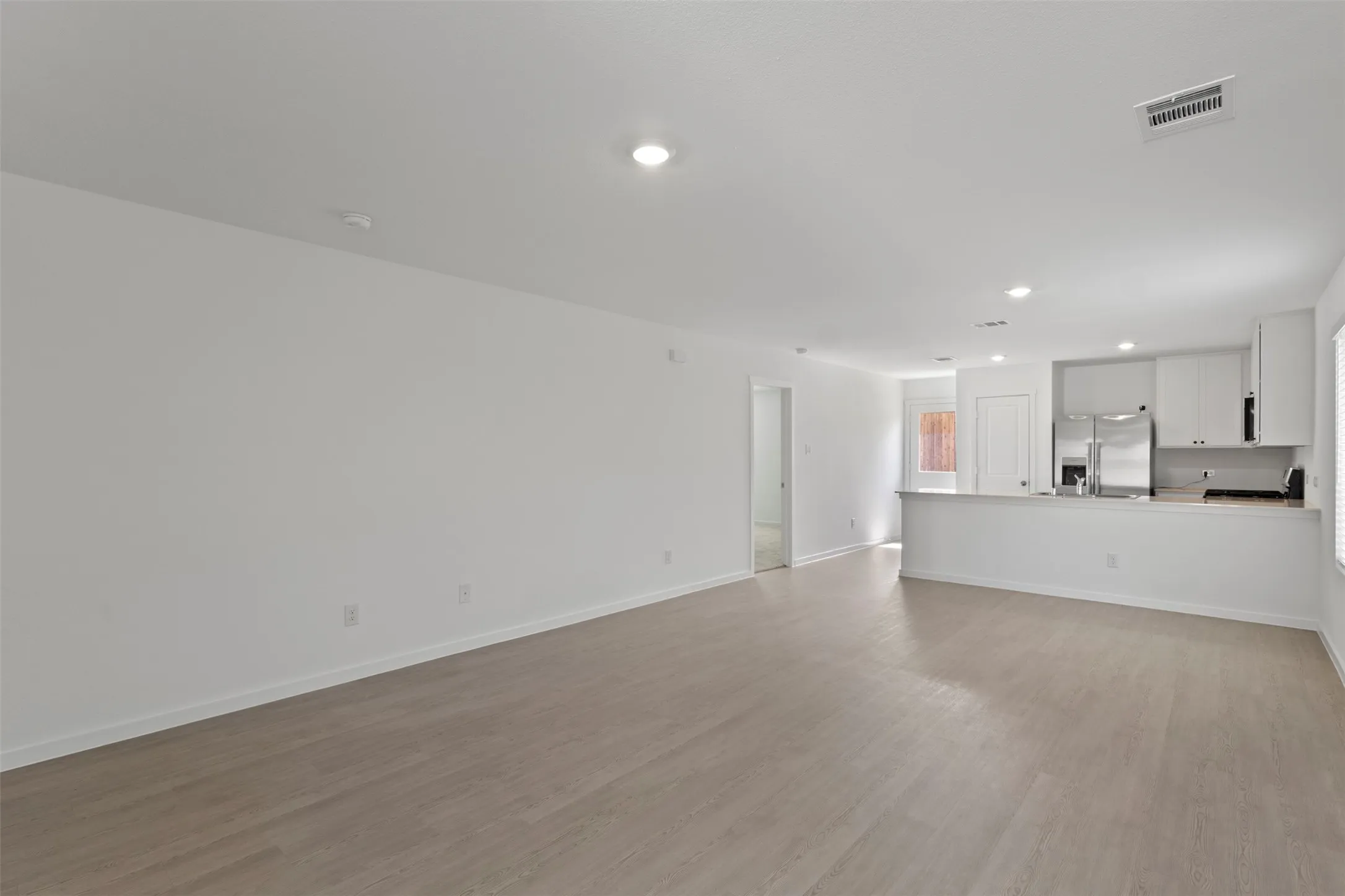 Open-concept living area featuring wood-finish flooring, recessed lighting, and a kitchen with stainless steel appliances, white cabinetry, and a peninsula