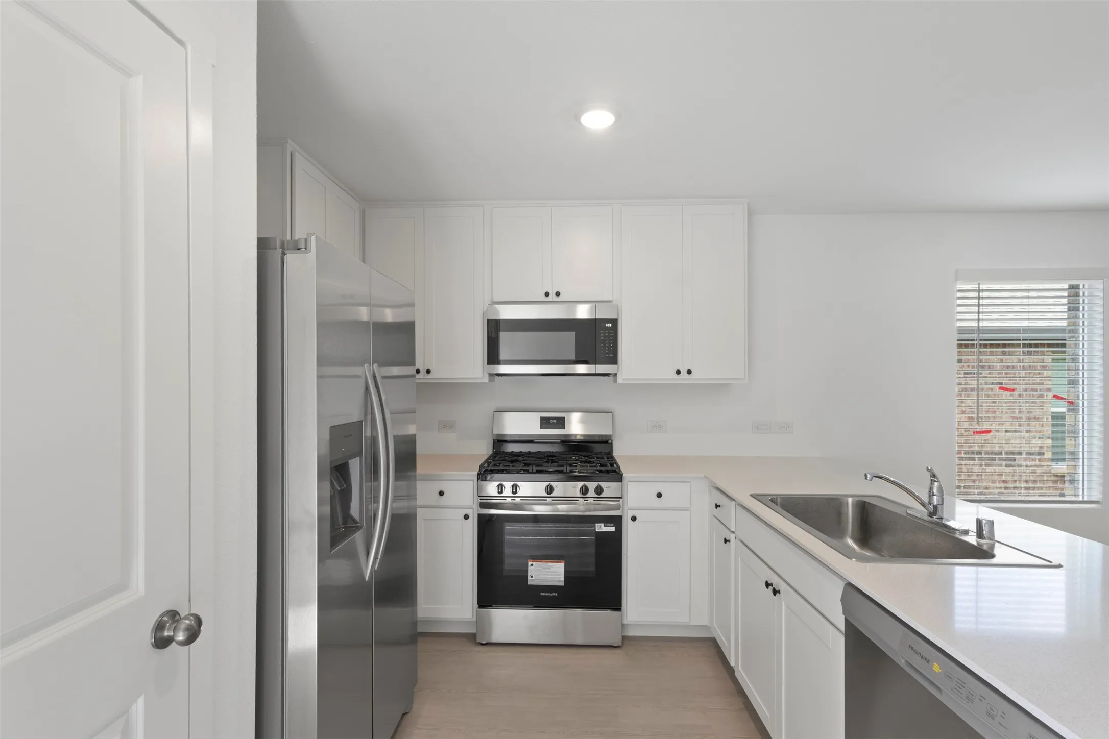 Kitchen featuring white cabinetry, stainless steel appliances, a stainless steel sink, light-toned countertops, and wood-finish flooring
