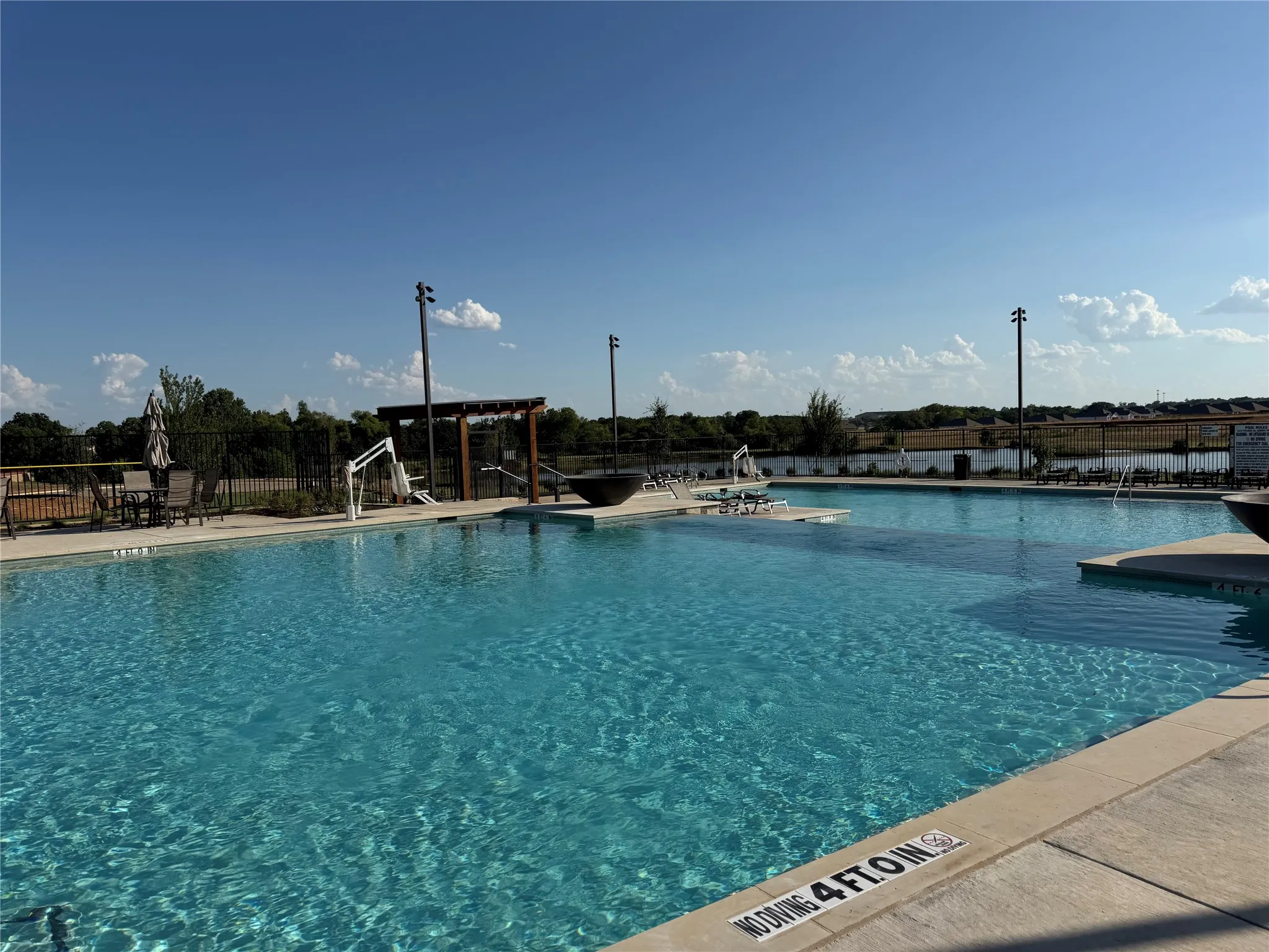 Expansive swimming pool with integrated shallow lounging areas, surrounding concrete decking, and a distant water feature