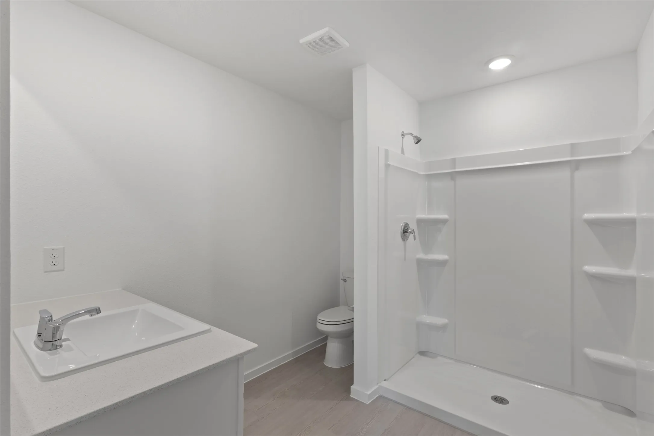 Compact bathroom featuring a shower with integrated shelving, a single-sink vanity with a chrome faucet, and light-toned flooring