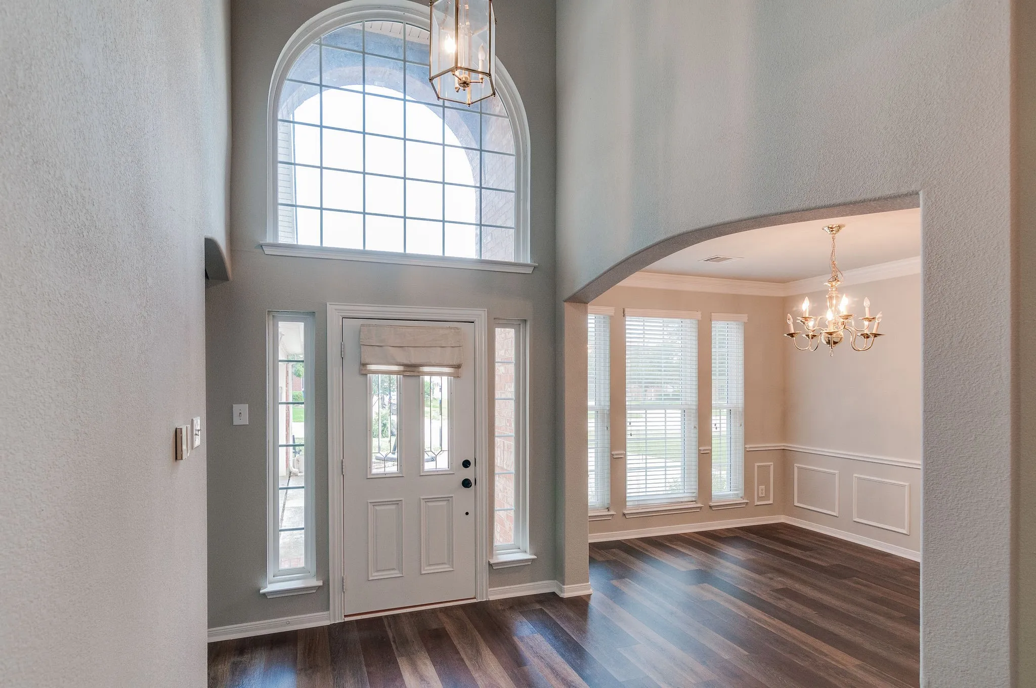 Two-story foyer with a large arched window, wood-finish flooring, and an arched entry to a room with crown molding, wainscoting, and a chandelier