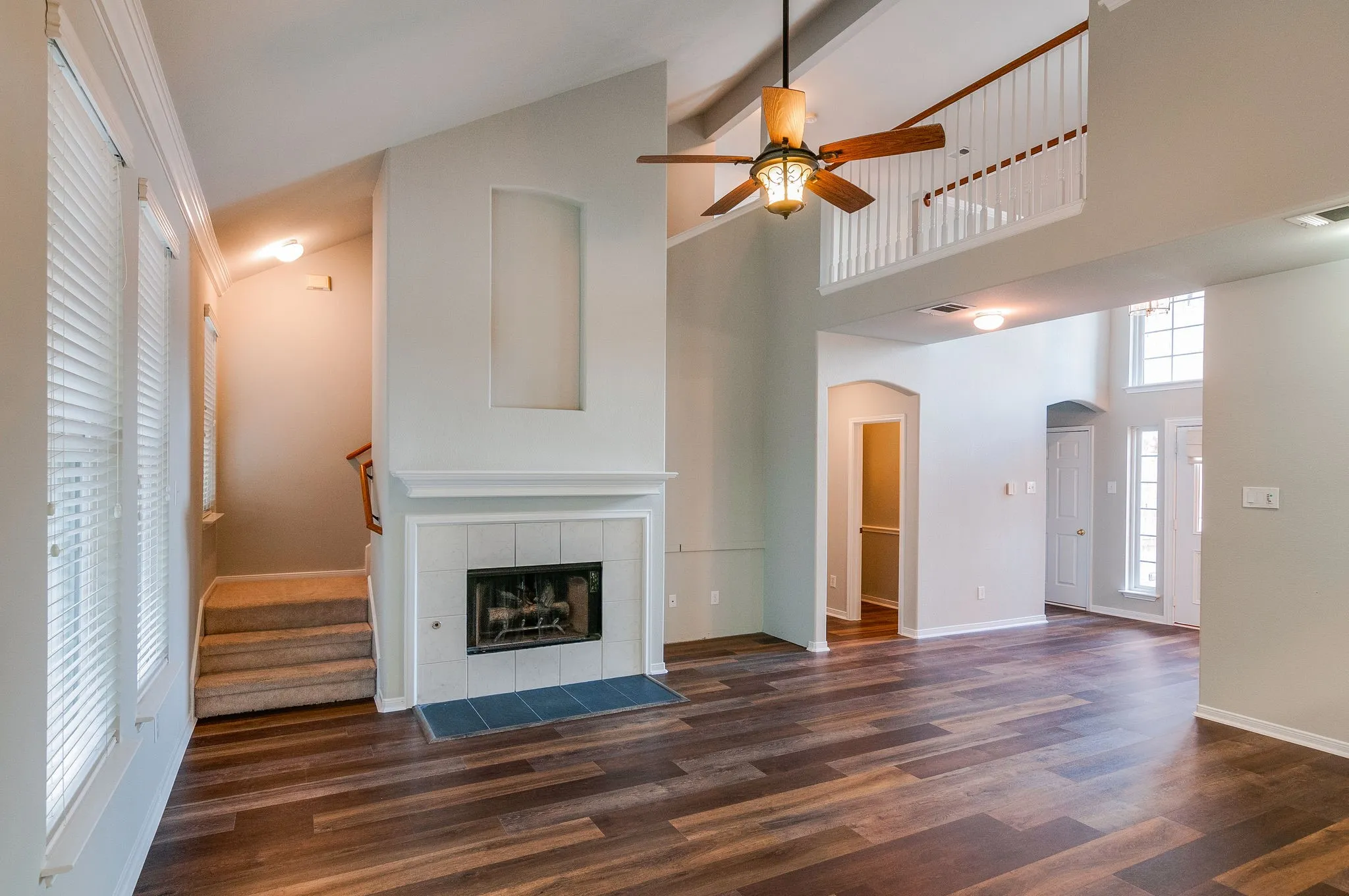 Vaulted ceiling with a ceiling fan, fireplace with a tile surround, wood-finish flooring, and a second-story landing with a white railing