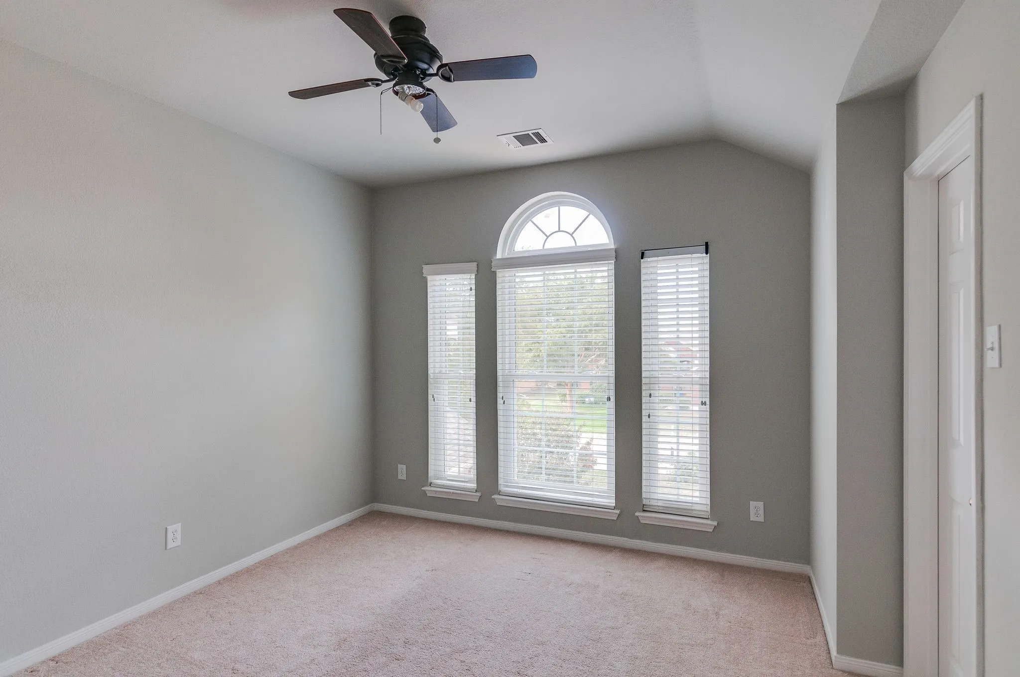 Vaulted ceiling with a ceiling fan, arched transom window, and carpet flooring