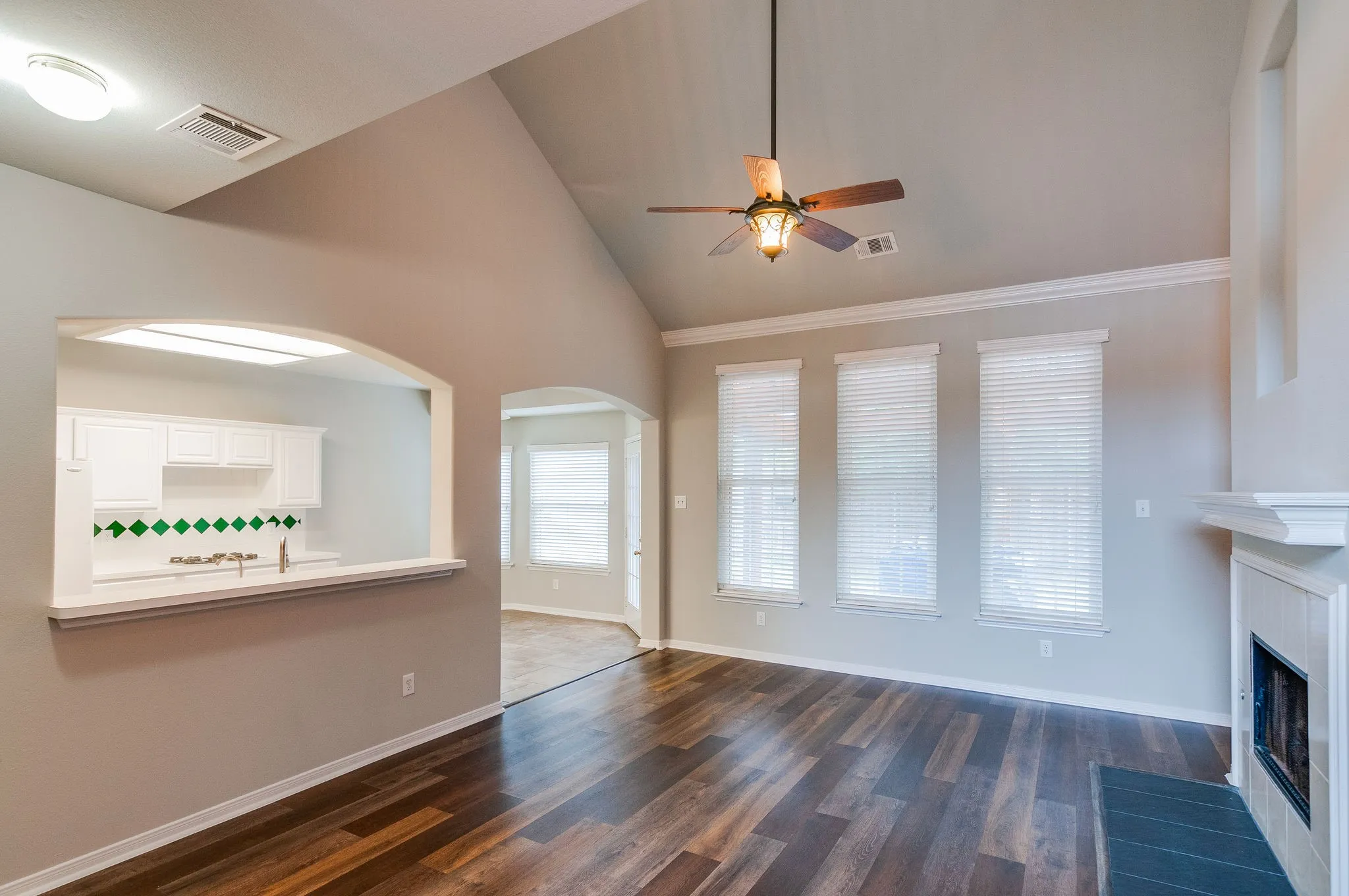 Vaulted ceiling with an installed ceiling fan, wood-finish flooring, and a fireplace with a white mantel