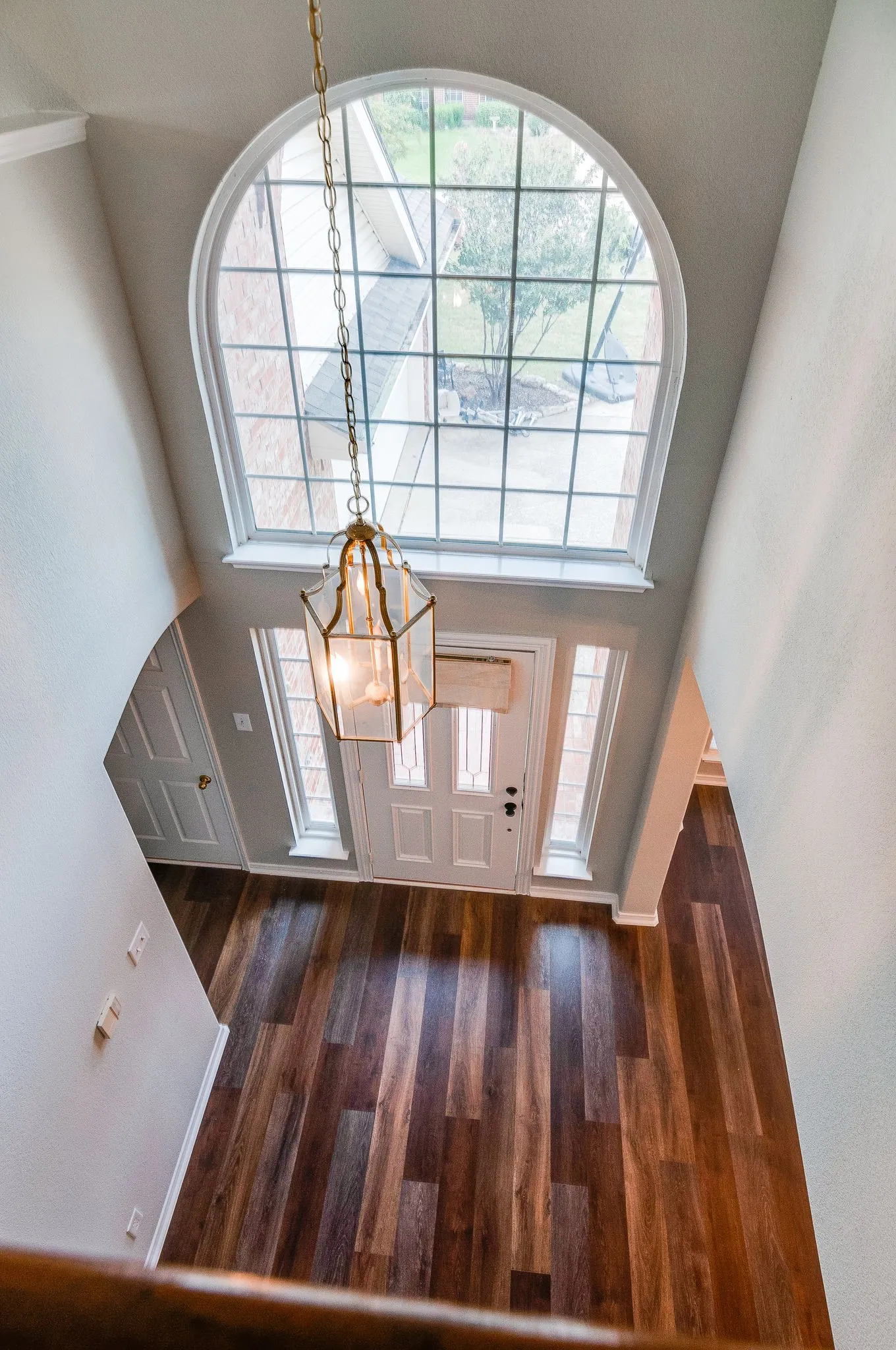 Two-story foyer featuring an arched window, wood-finish flooring, a decorative chandelier, and a panel door with sidelights