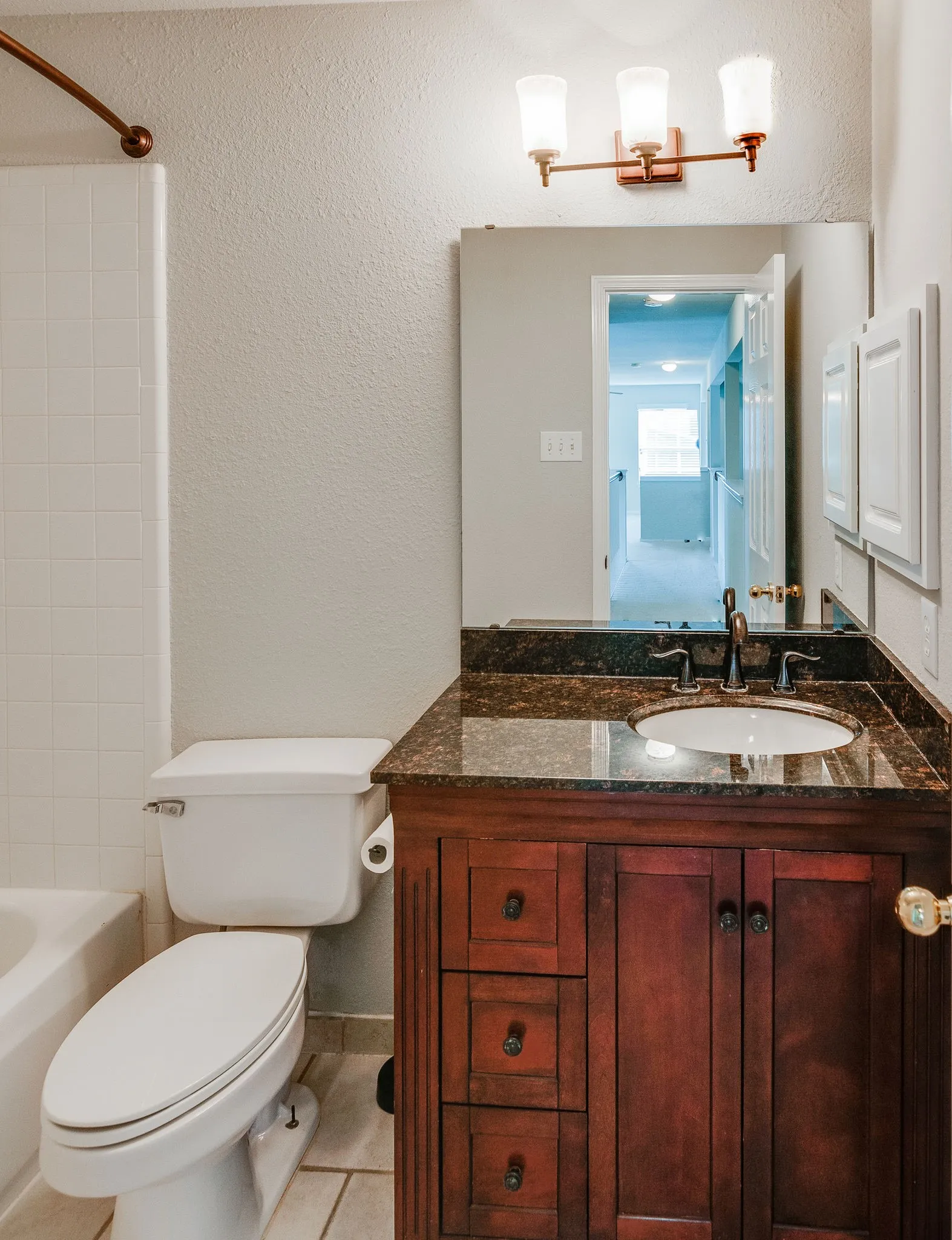 Dark wood-finish vanity with an integrated sink, dark stone-finish countertop, and bronze-finish faucet