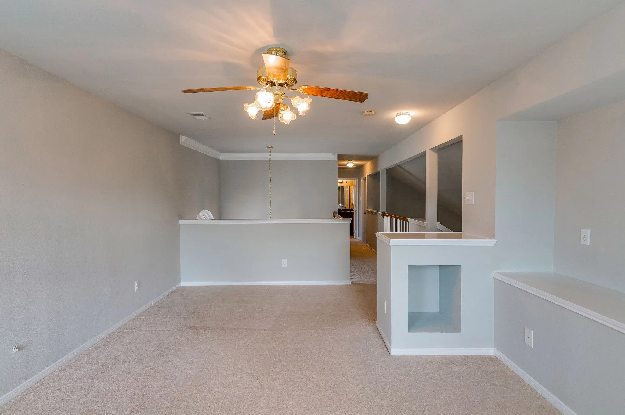 Carpeted open-concept room with a ceiling fan light fixture, crown molding, and an integrated display niche