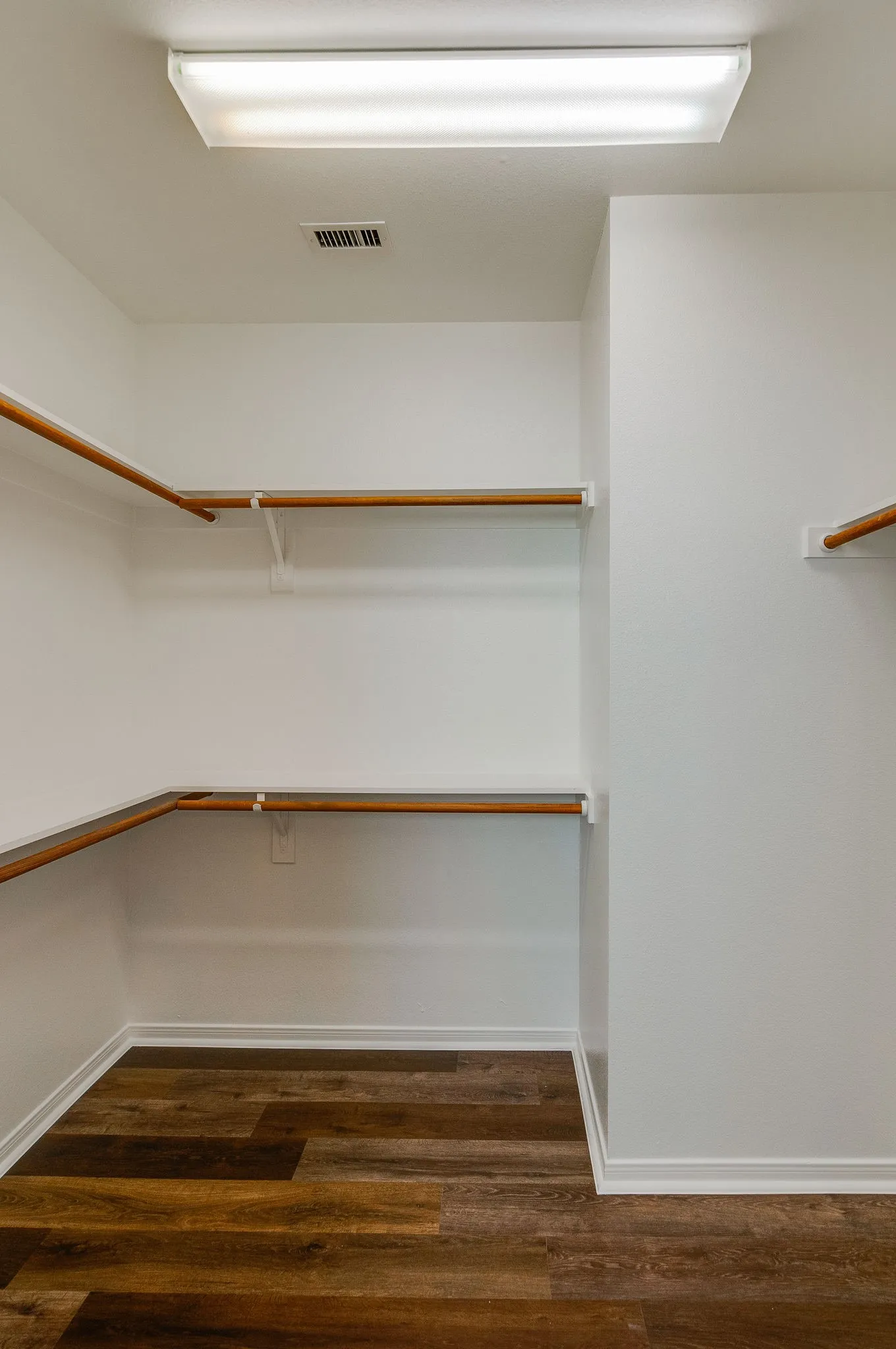 Spacious walk-in closet featuring multiple wood-finish hanging rods, recessed ceiling lighting, and rich wood-finish flooring throughout