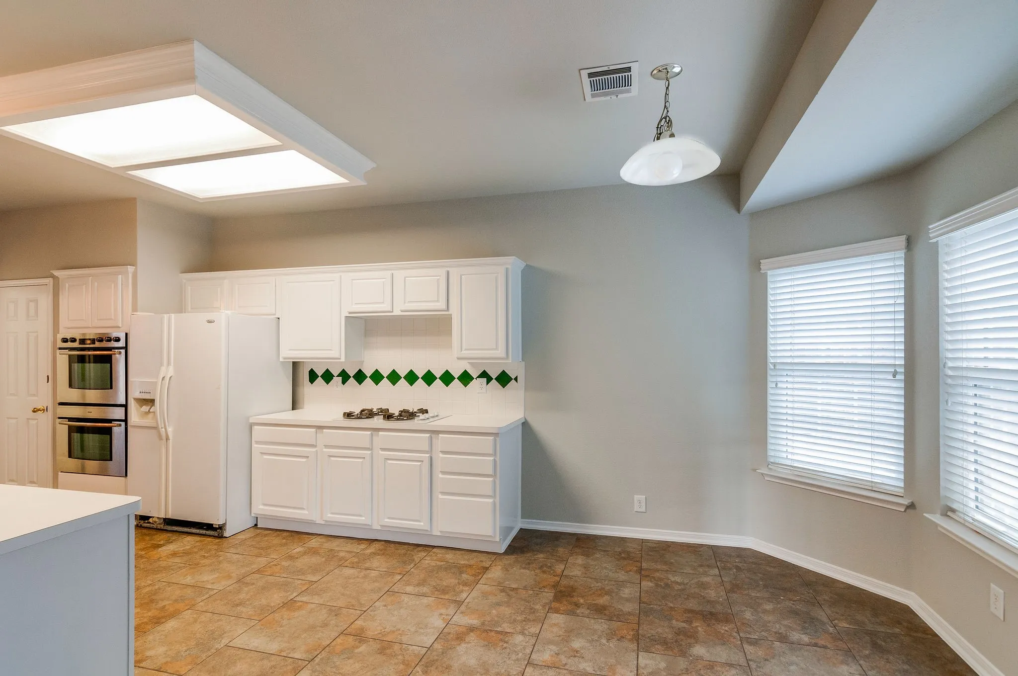 Spacious kitchen area featuring white cabinetry, tile flooring, and integrated double ovens