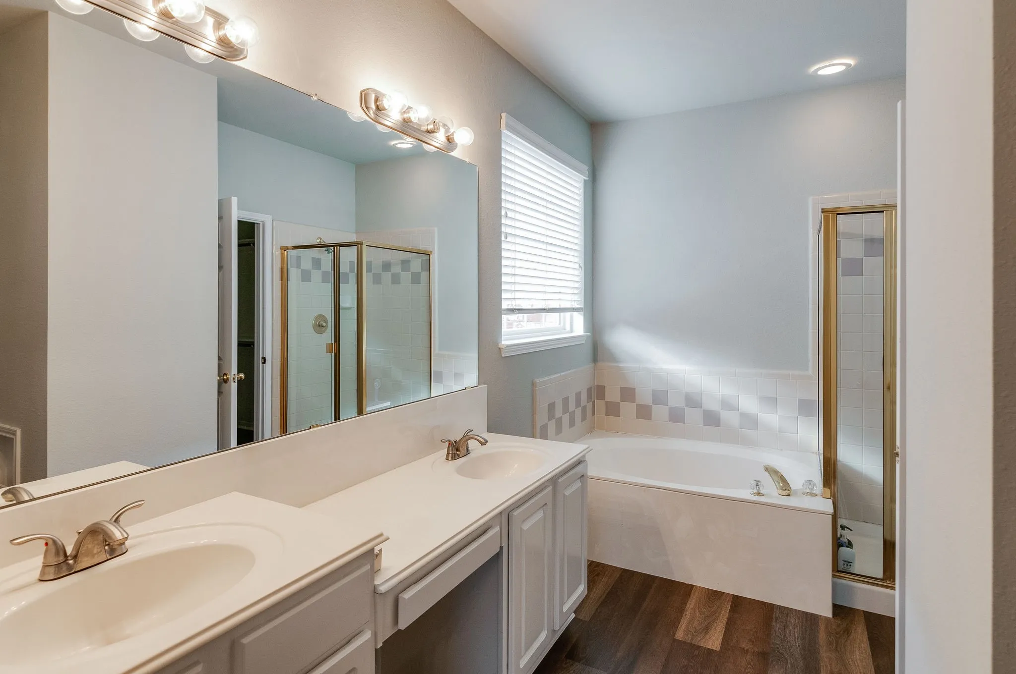 Dual vanity with integrated sinks, wood-finish flooring, built-in bathtub, and a glass-enclosed shower