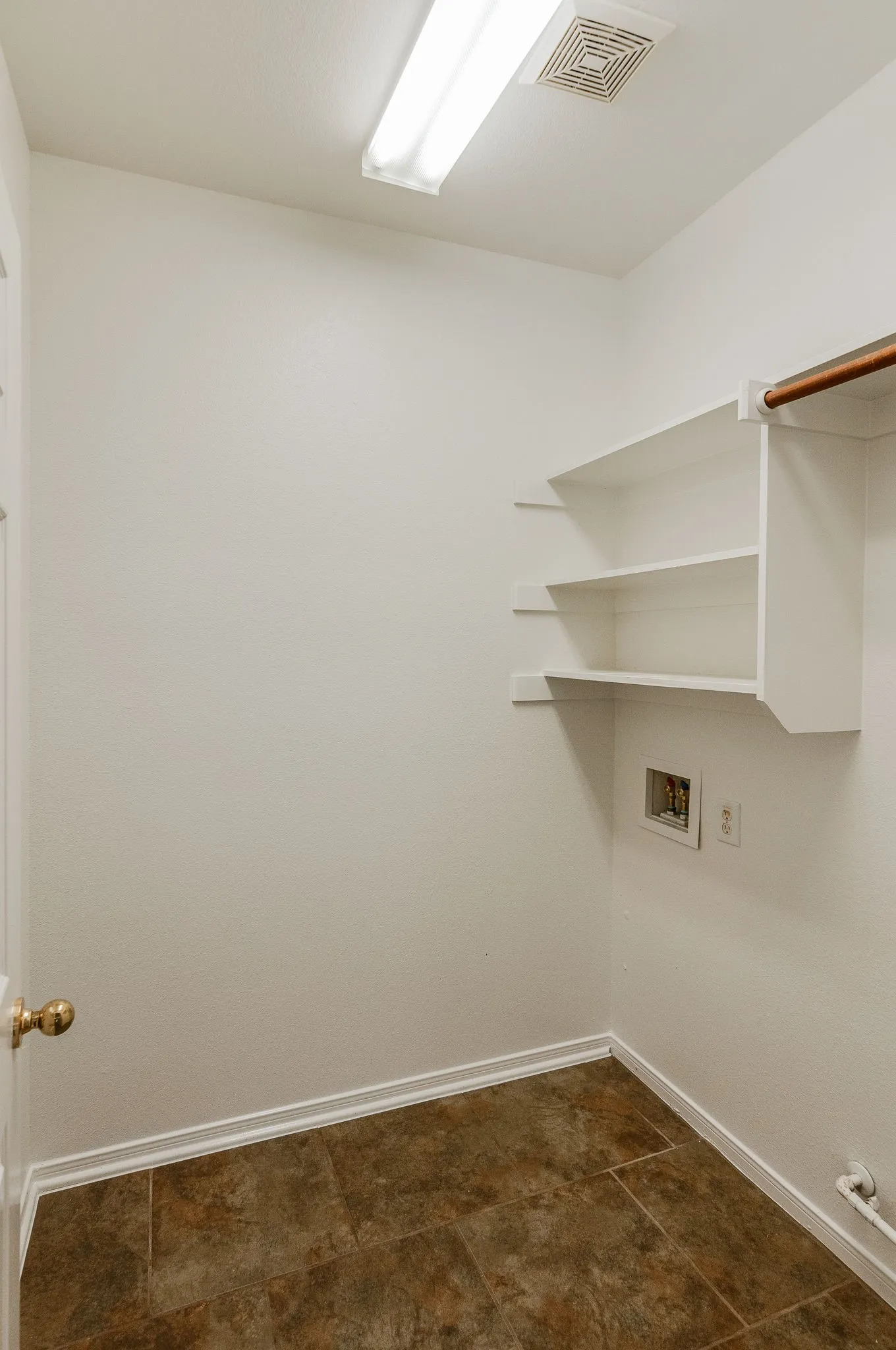 Utility room featuring built-in shelving, a clothes hanging rod, tile flooring, and overhead lighting