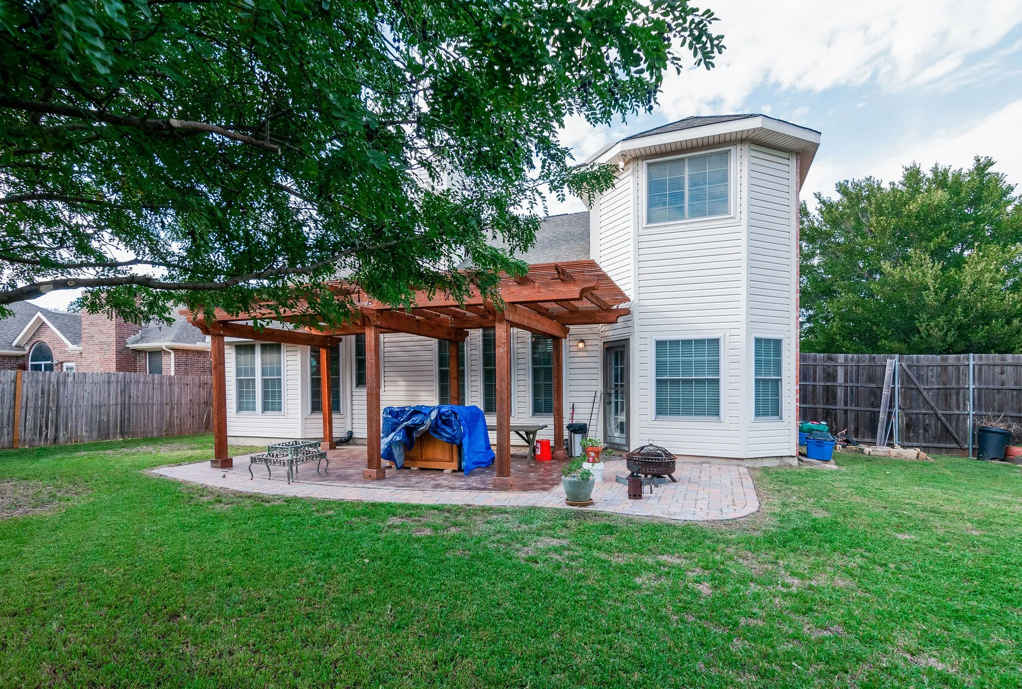 Expansive backyard featuring a manicured lawn, a wood pergola over a paver patio, and a privacy fence