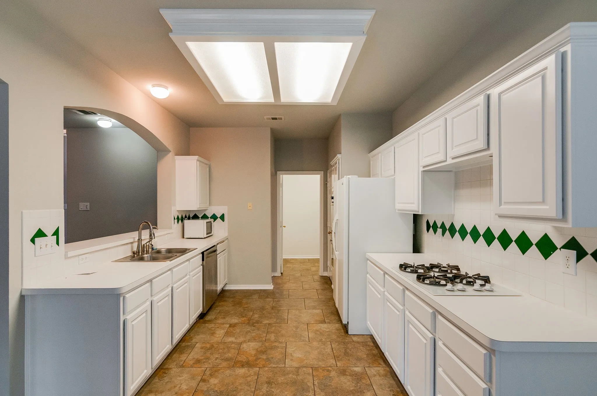 Galley kitchen featuring white cabinetry, light countertops, tile flooring, and a gas cooktop