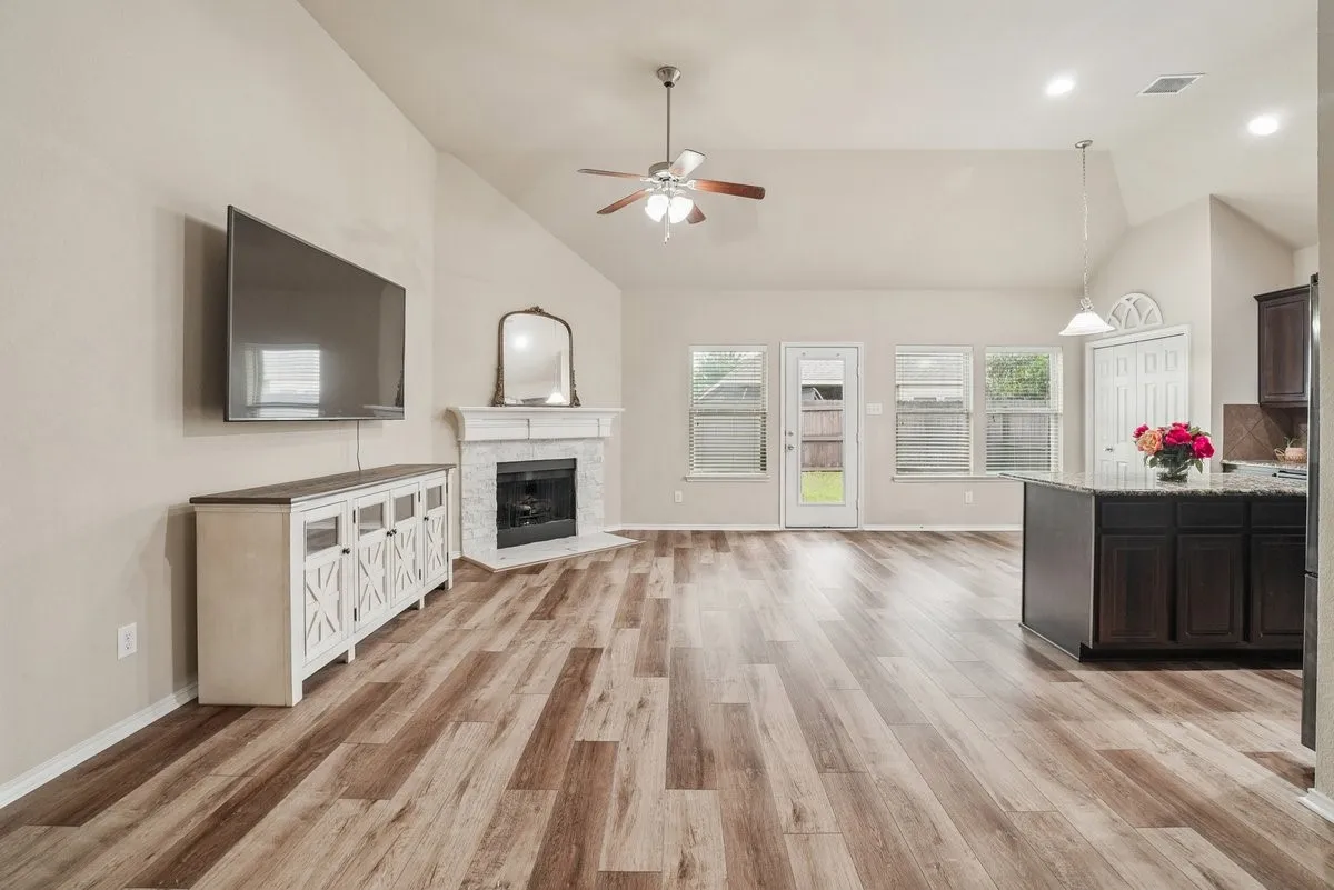 Vaulted ceiling, wood-finish flooring, fireplace with stone surround, recessed lighting, and kitchen island with granite-style countertop
