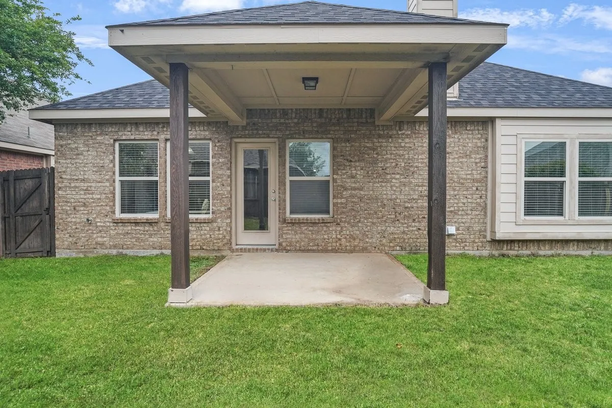Covered patio with a concrete slab, supported by wood columns, featuring a brick exterior and multiple windows
