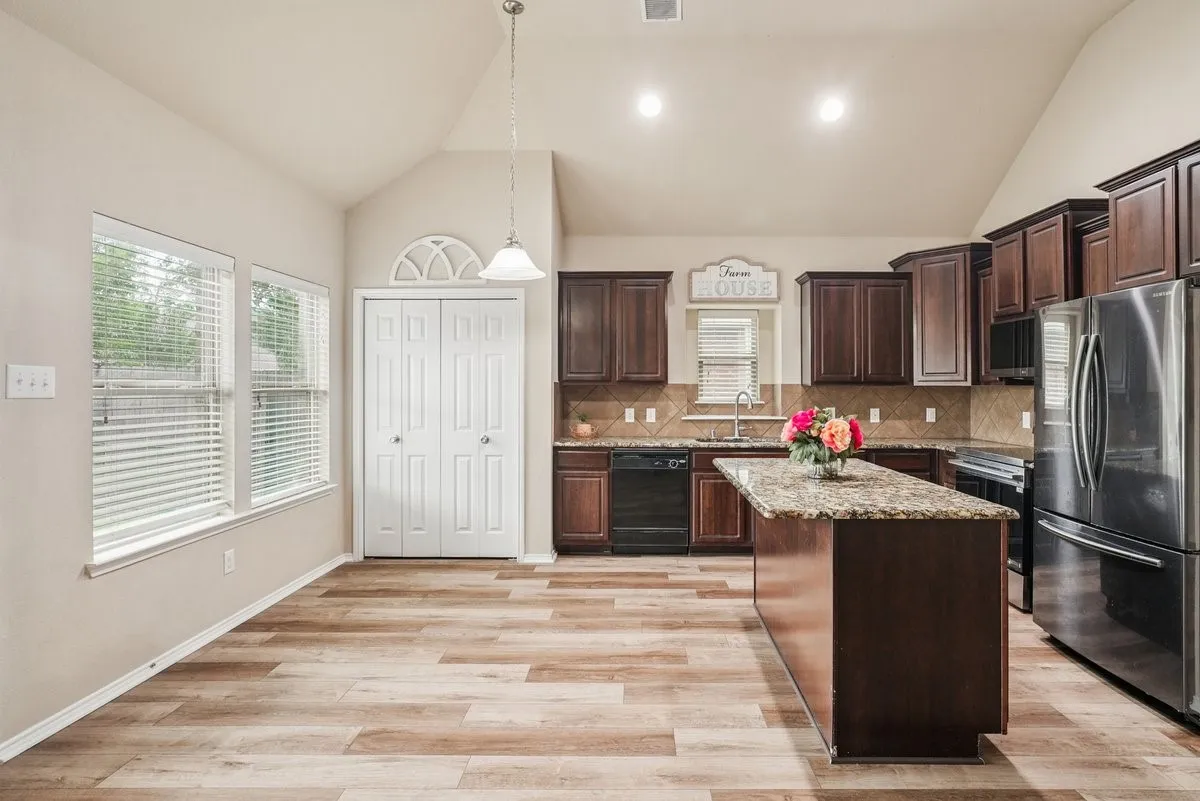 Vaulted ceiling, wood-finish flooring, two large windows, kitchen island with stone countertop, and stainless steel appliances