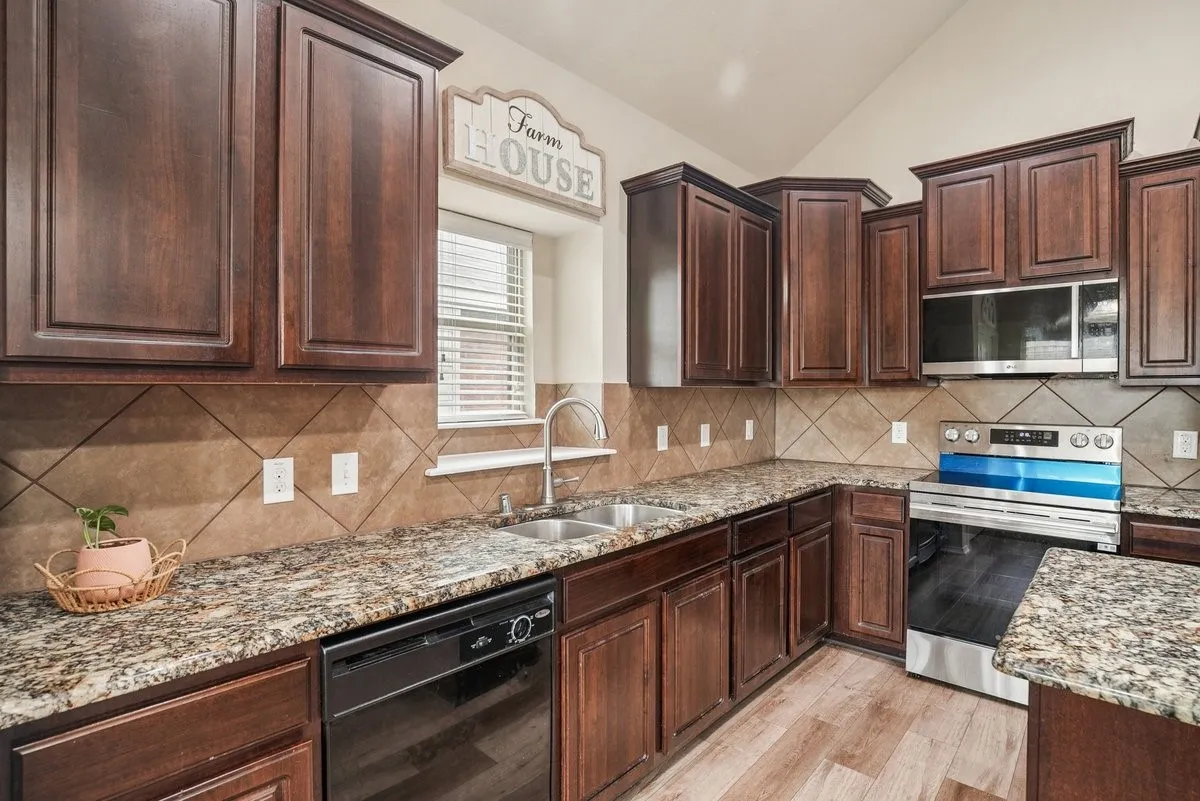 Kitchen with rich wood-finish cabinetry, granite-style countertops, stainless steel appliances, a double basin sink, and wood-finish flooring