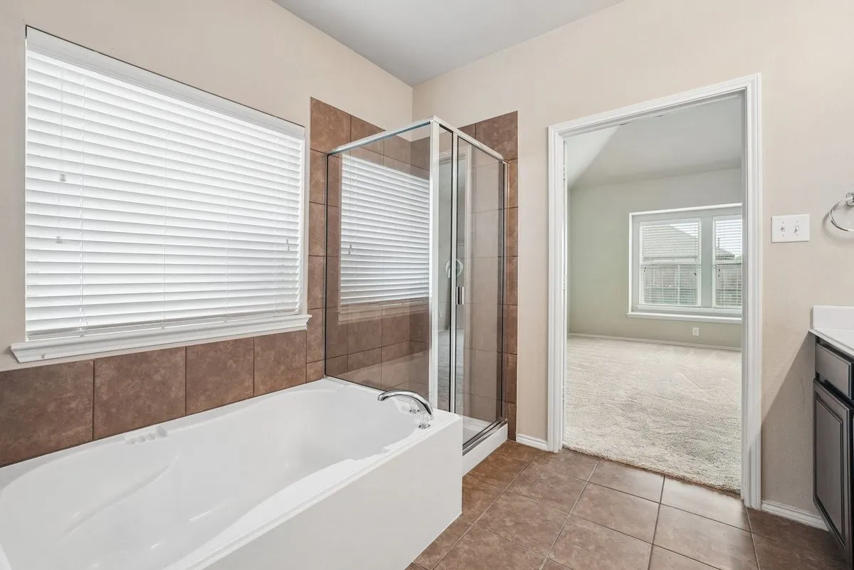 Recessed bathtub with chrome fixtures, glass-enclosed shower, and tile surround