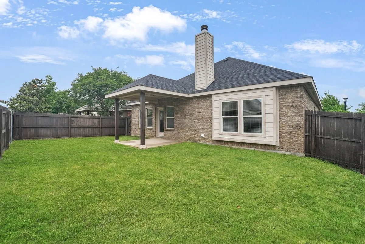 Expansive grassy yard with full privacy fencing, brick exterior, covered patio, and a prominent chimney