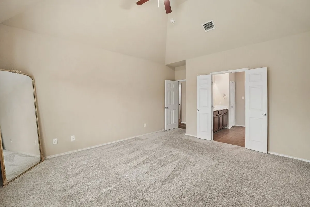 Vaulted ceiling with an attached ceiling fan, neutral wall tones, light gray carpet, and white paneled doors