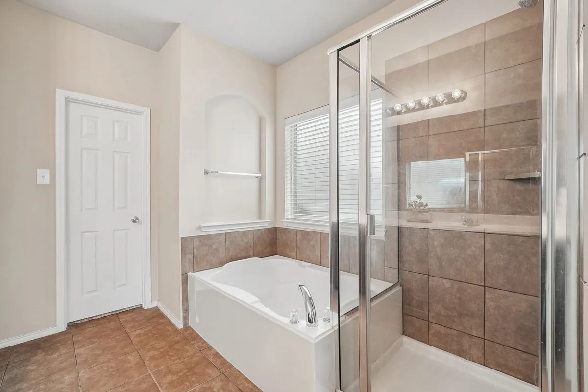 Bathroom featuring a built-in tub, separate glass-enclosed shower with tile surround, and tile flooring