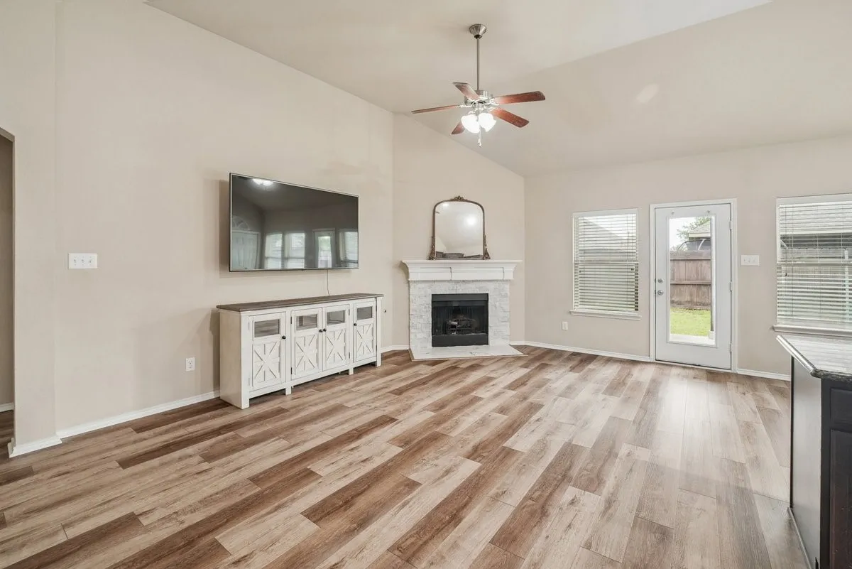 Vaulted ceilings, wood-finish flooring, ceiling fan, fireplace with a mantle, and a glass-paneled exterior door