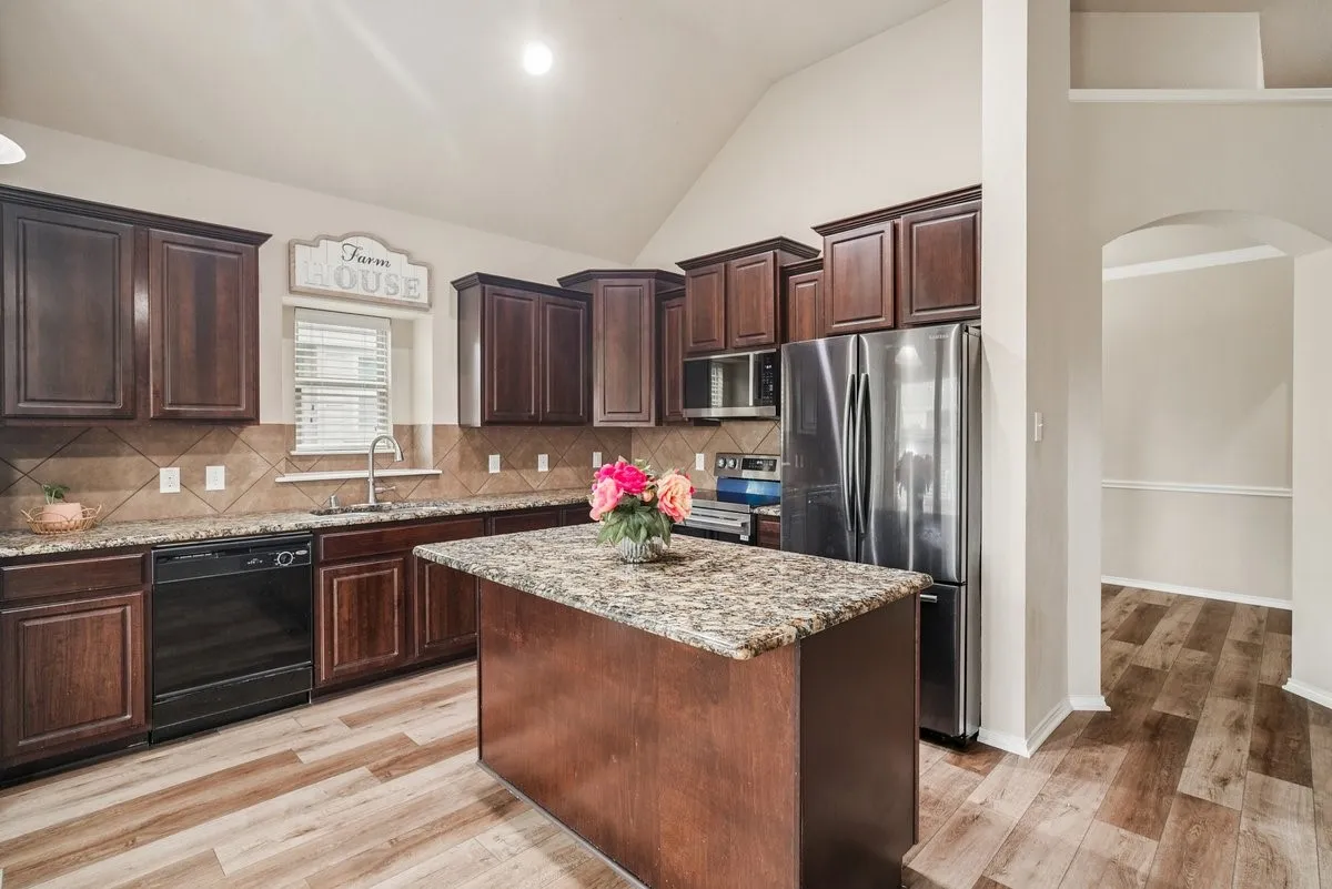 Kitchen featuring wood-finish flooring, vaulted ceiling, wood cabinetry, stone countertops, and stainless steel appliances