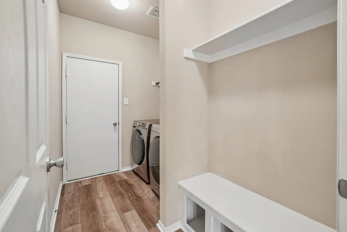 Laundry area featuring wood-finish flooring, a built-in bench with storage, and an overhead shelf