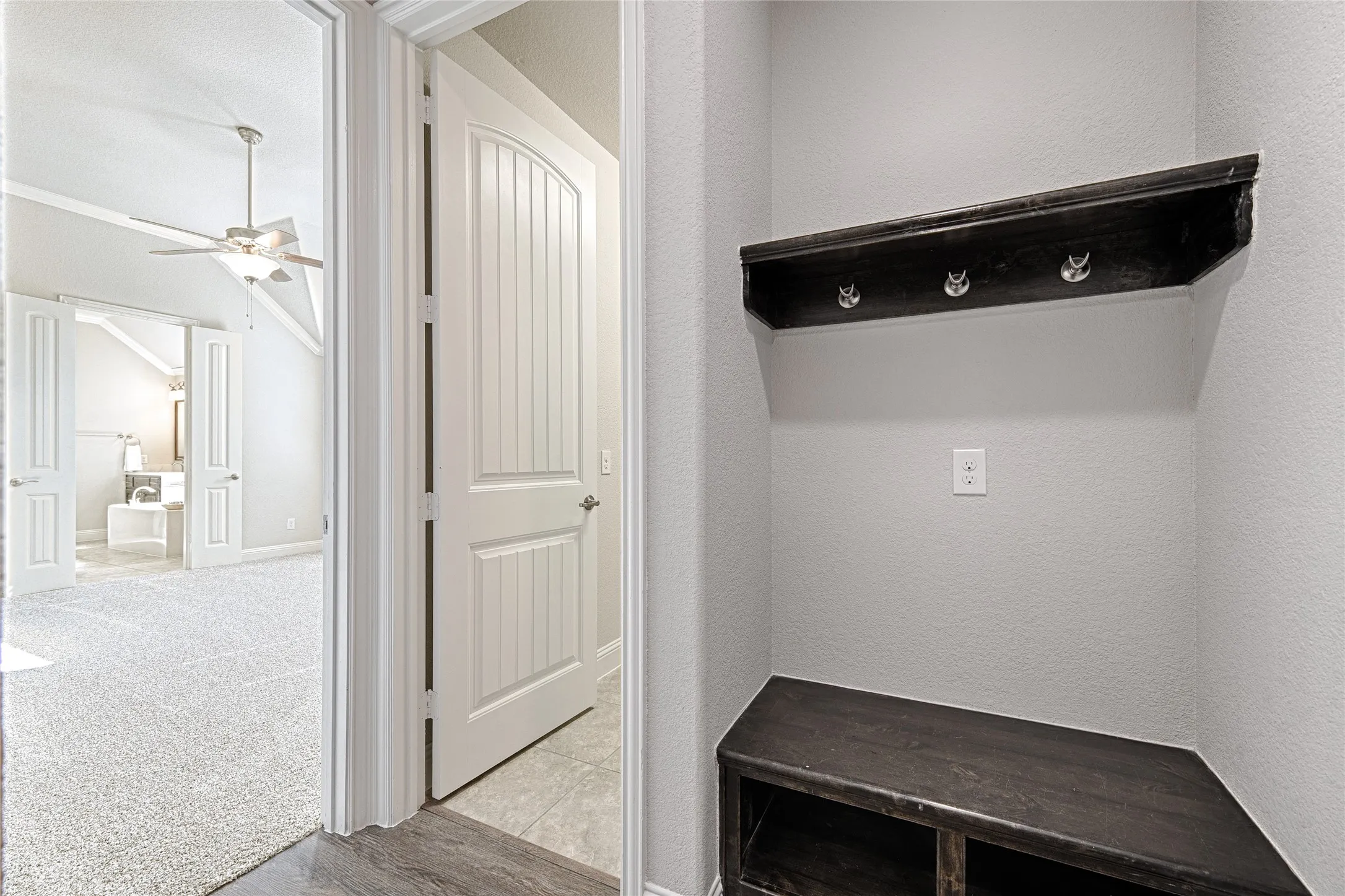Built-in corner bench with storage, dark wood-finish shelving with coat hooks, white paneled doors, and vaulted ceiling with ceiling fan