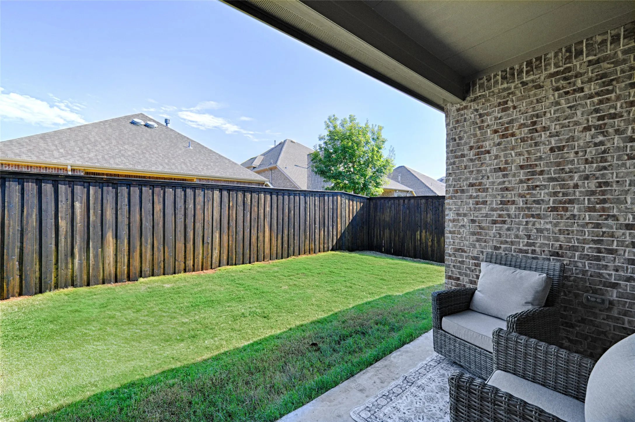 Covered patio with a concrete surface, a brick exterior wall, and a wood privacy fence enclosing a grass lawn
