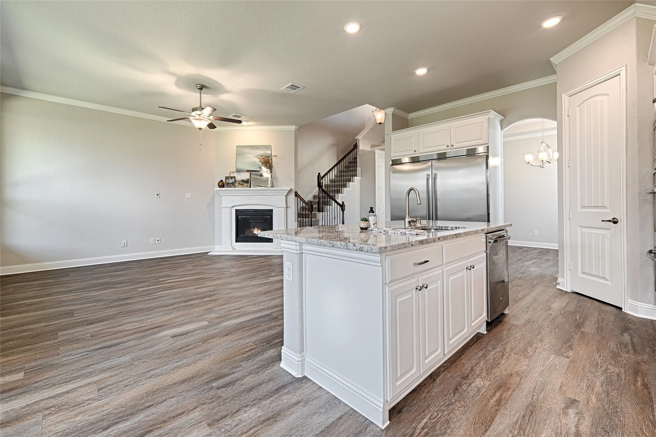 Open-concept living area featuring wood-finish flooring, a white fireplace, and crown molding
