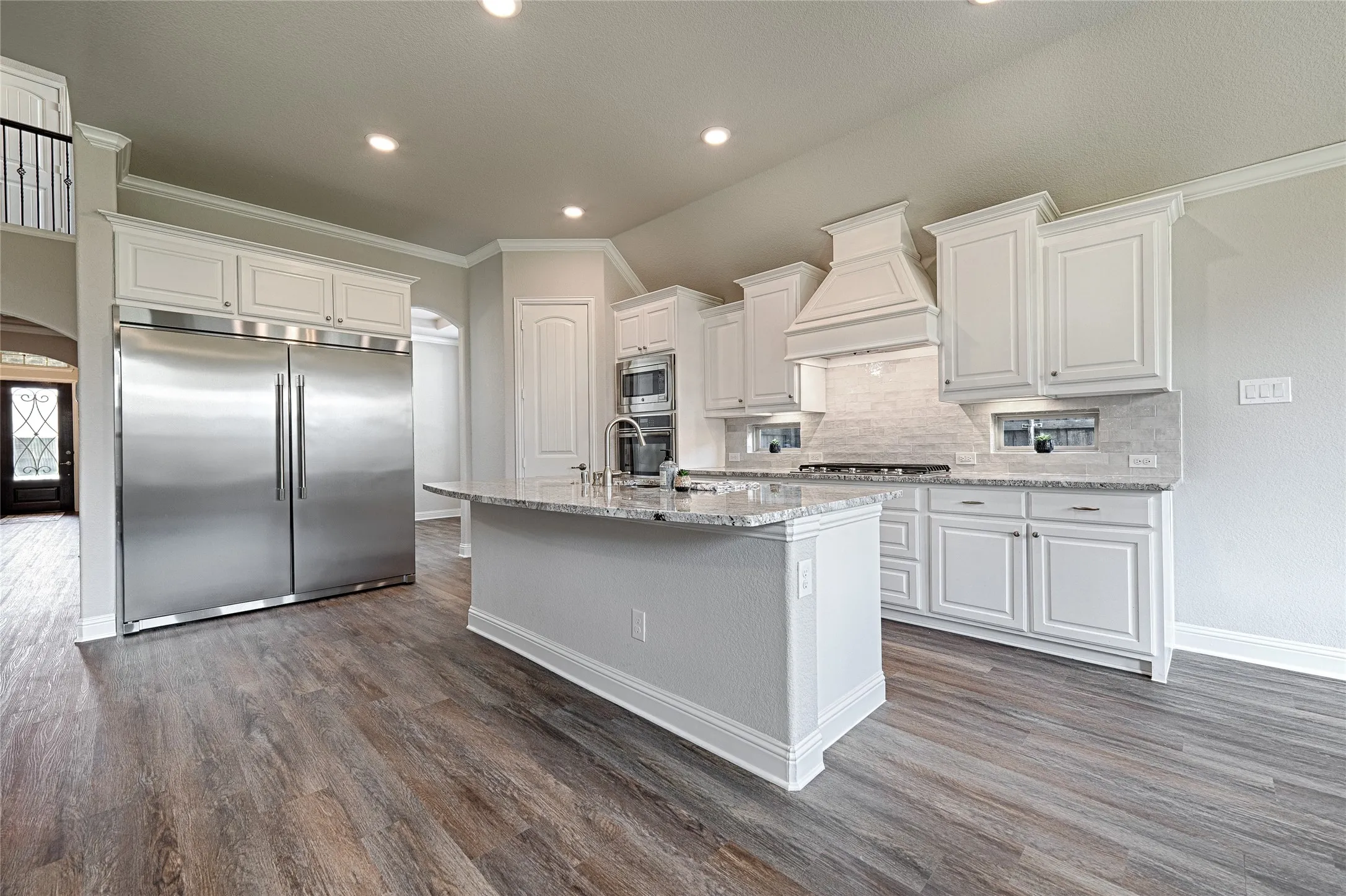 Spacious kitchen featuring an expansive center island, white cabinetry, integrated stainless steel appliances, wood-finish flooring, and recessed lighting