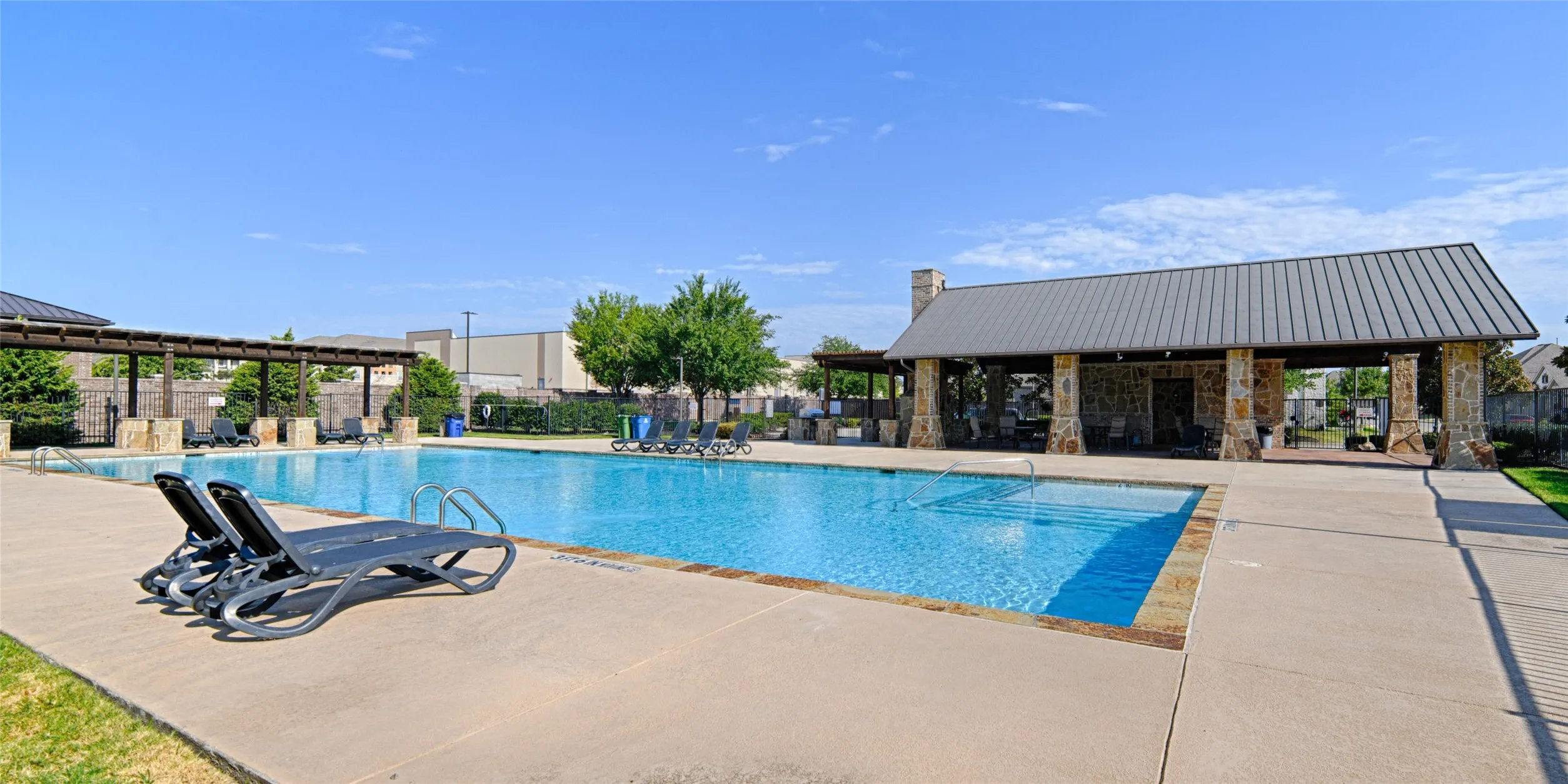 Spacious community pool with an adjacent stone-clad pavilion featuring a gabled metal roof