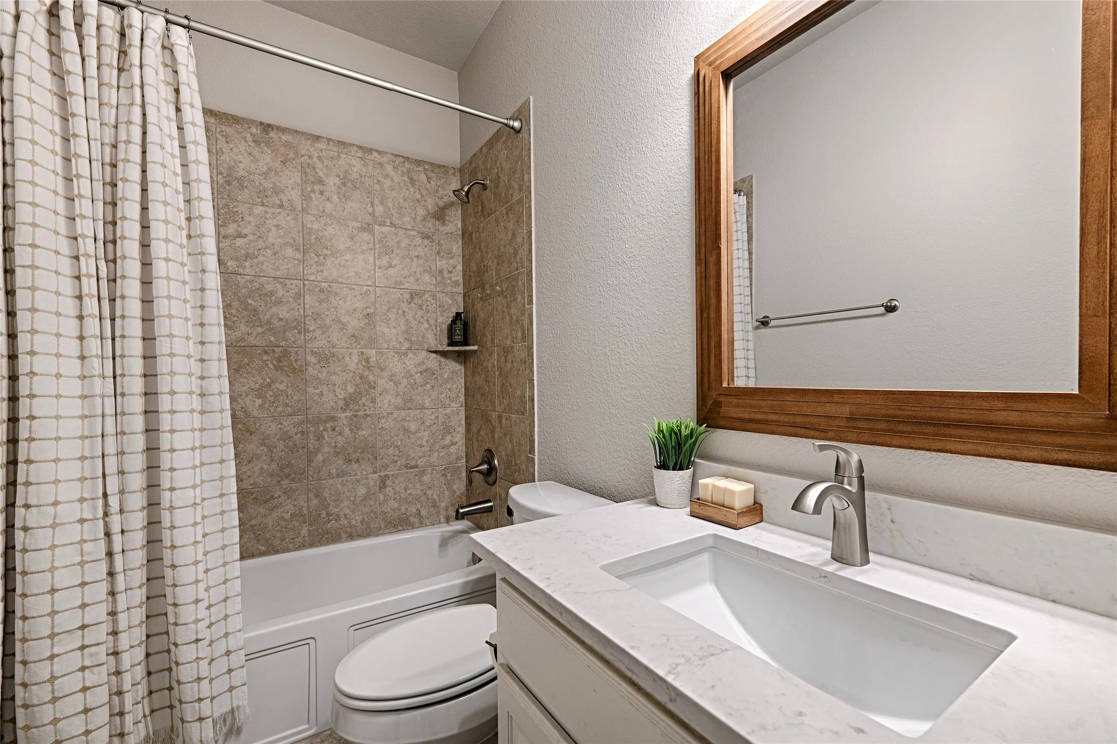 Bathtub with tiled surround, built-in shelving, white vanity with integrated sink, light-toned countertop, and wood-framed mirror