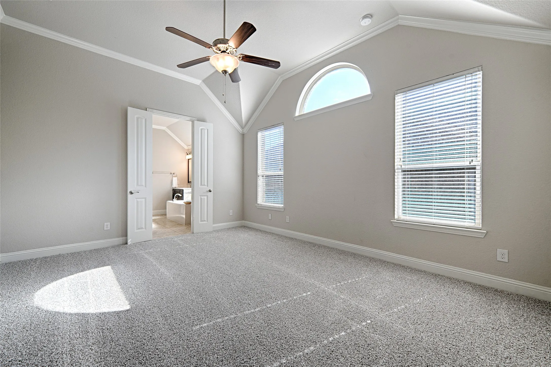 Primary bedroom, Vaulted ceiling with crown molding, ceiling fan, and arched transom window
