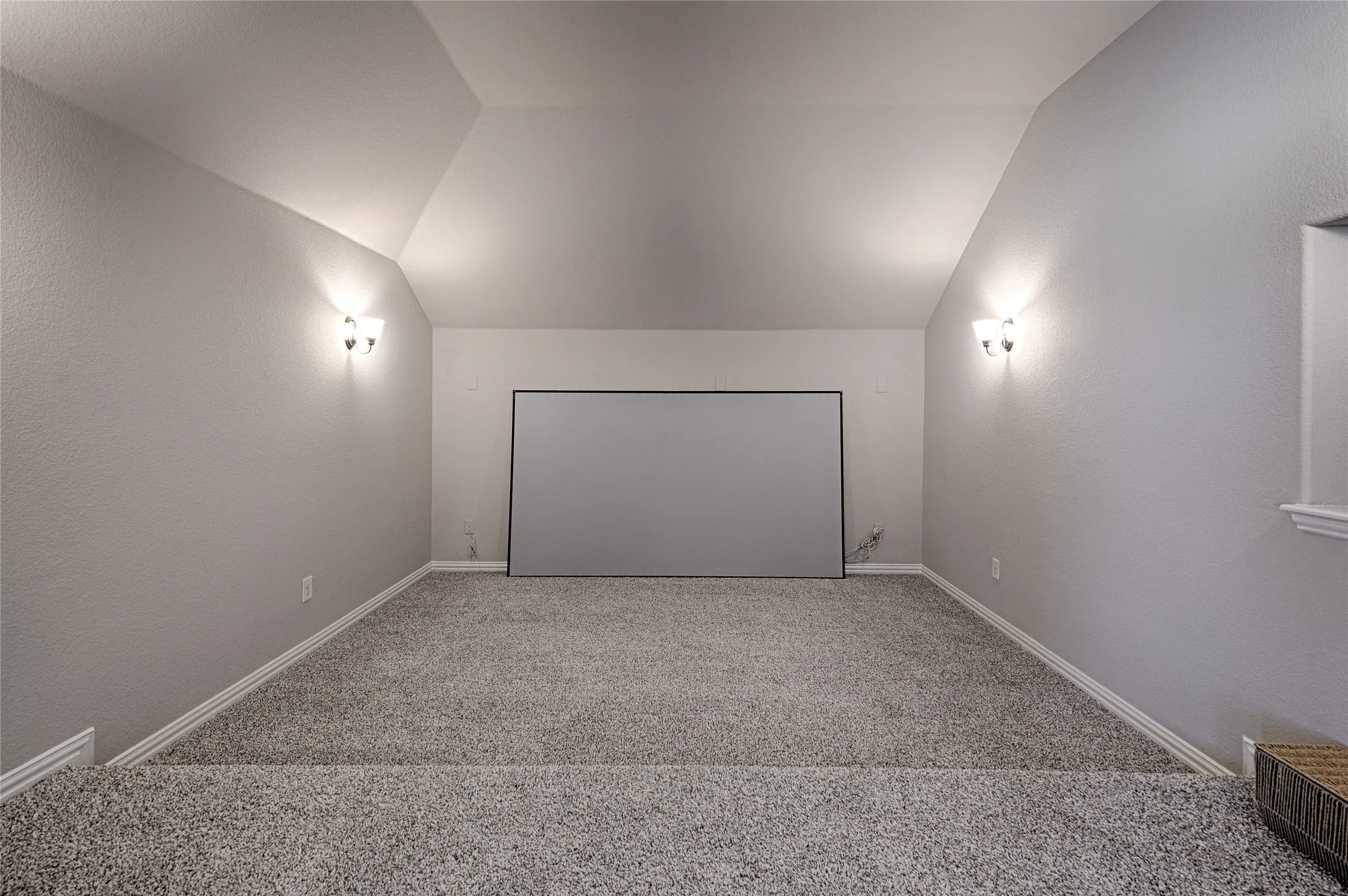 Carpeted media room featuring a projection screen, vaulted ceiling, and dual wall sconces