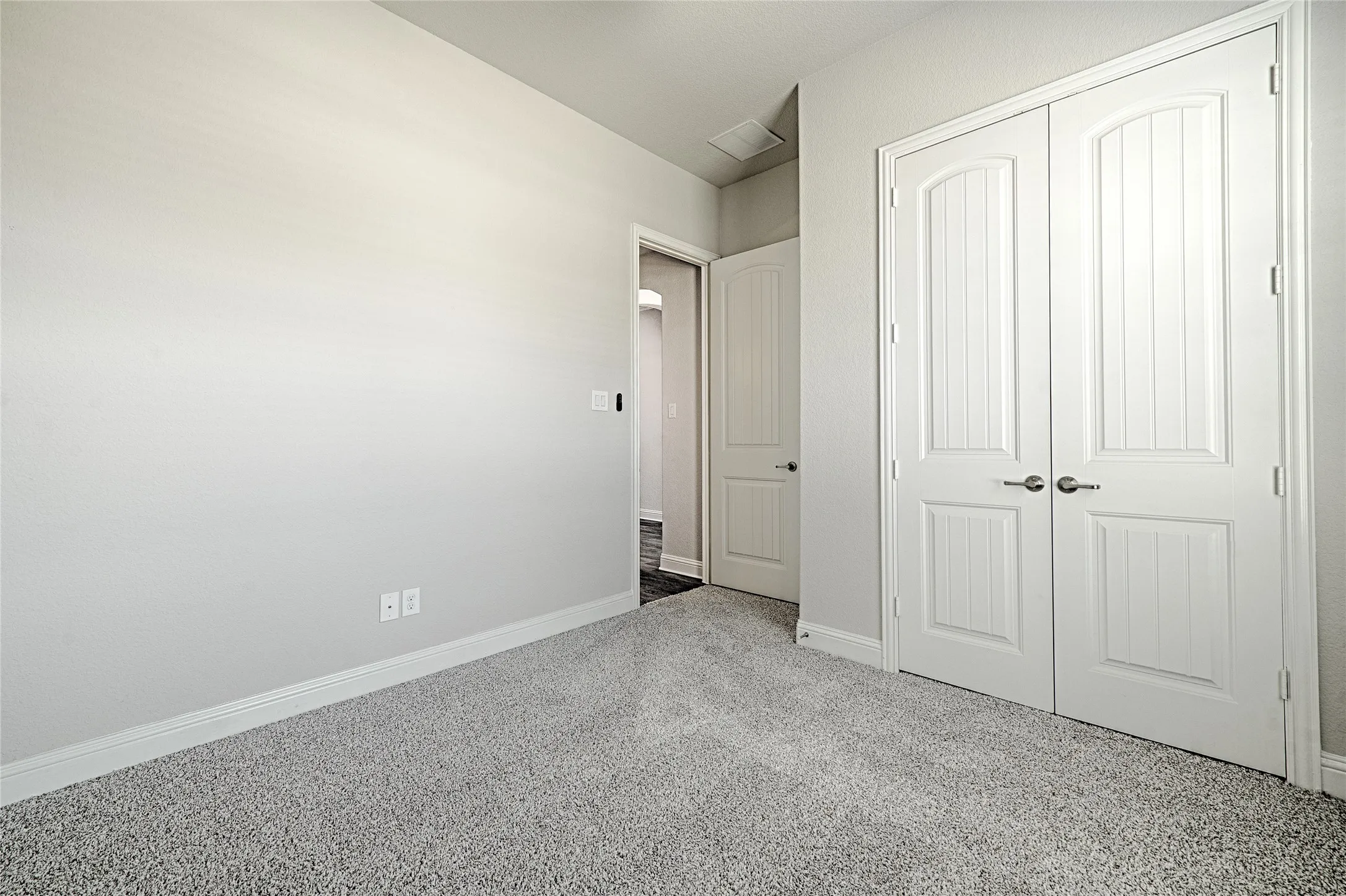 Light gray carpeted flooring, white painted walls, and double bifold doors with brushed nickel hardware