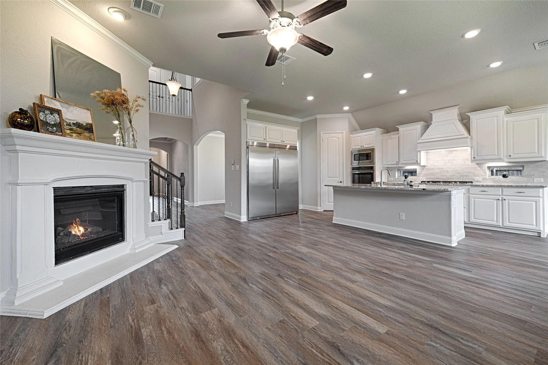 Open-concept living space featuring wood-finish flooring, a white mantel fireplace, and a kitchen island with seating