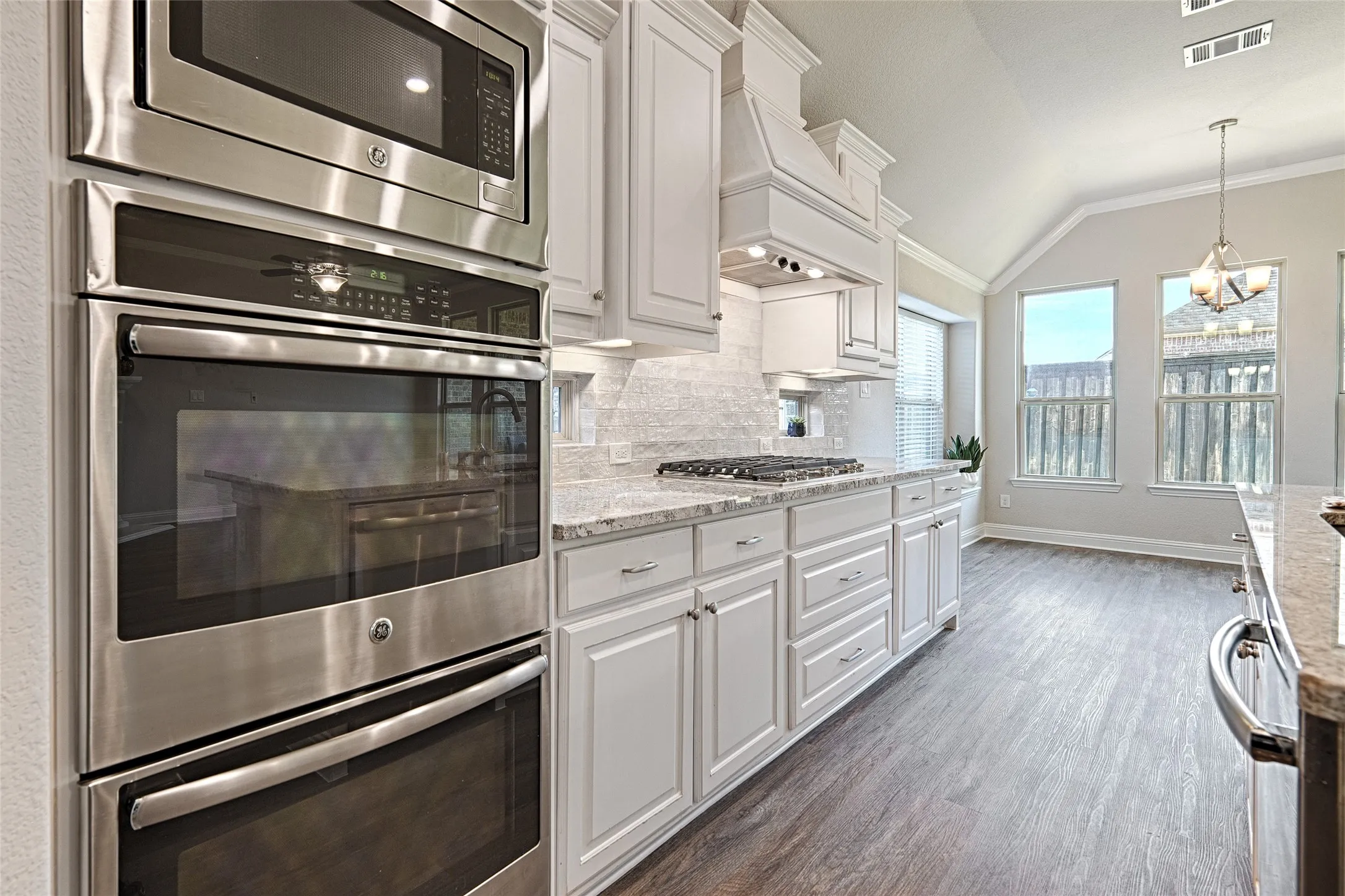 White cabinetry, stainless steel appliances, granite countertops, tile backsplash, and wood-finish flooring