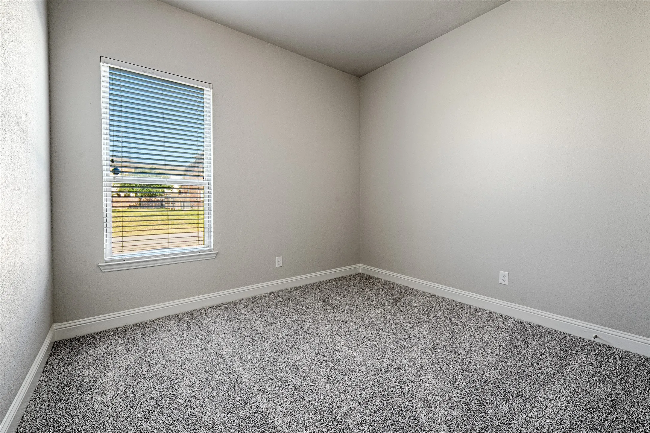 Secondary bedroom with new carpet, textured walls, white trim, grey patterned carpet, and window with white blinds