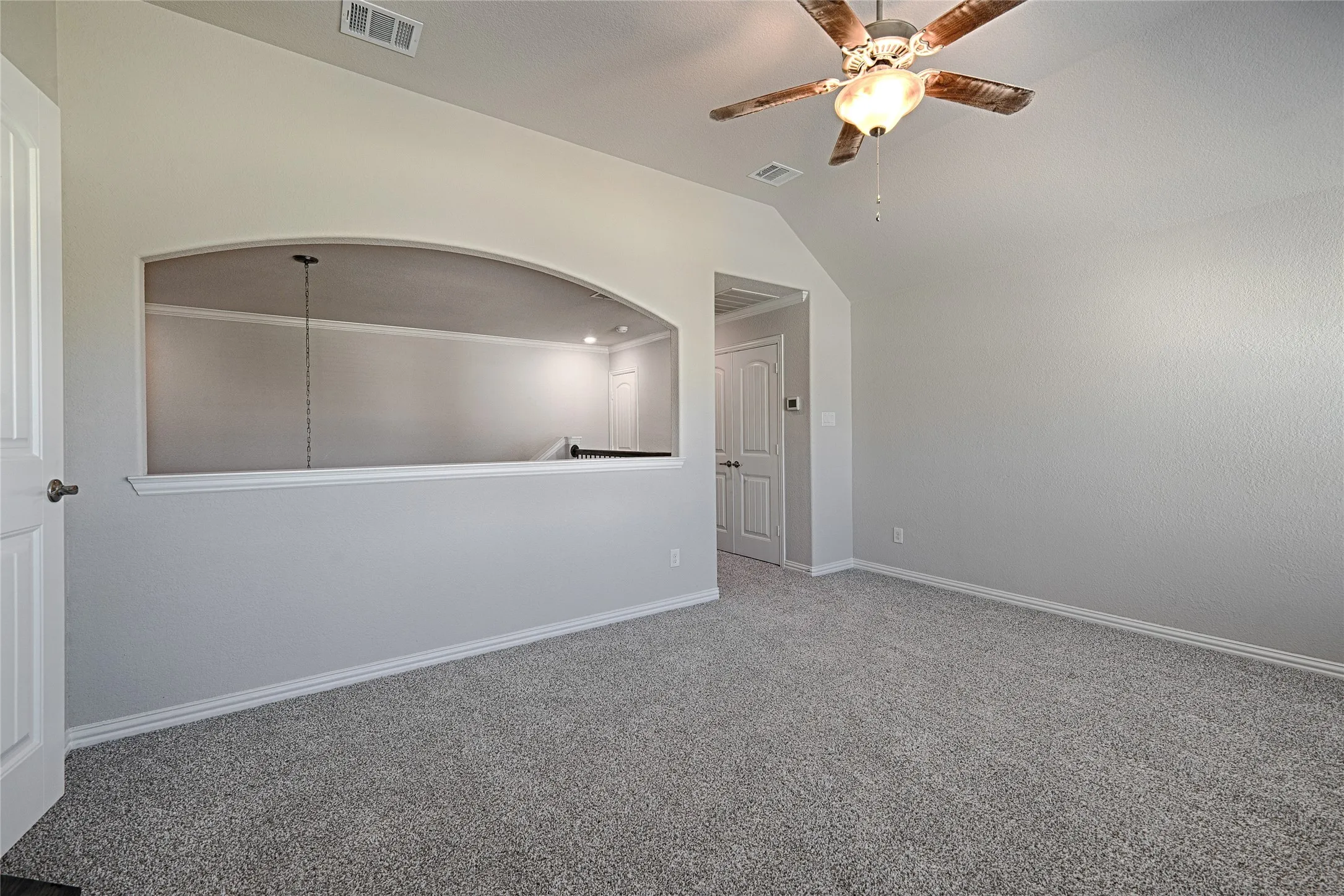 Neutral-toned carpeting, vaulted ceiling, built-in architectural archway, and overhead ceiling fan with light fixture