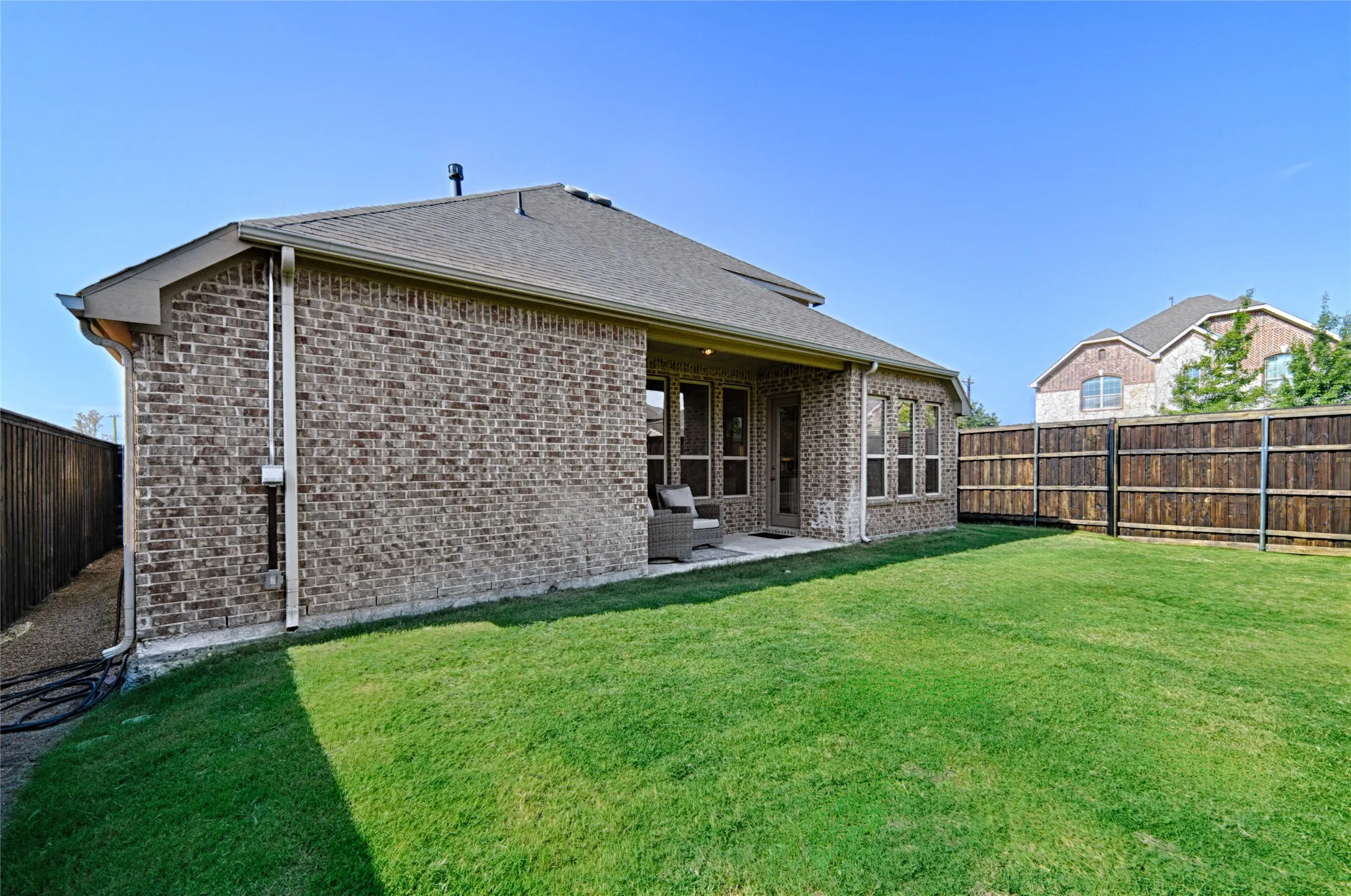 Backyard featuring a manicured lawn, full brick exterior, a covered patio, and a wood privacy fence