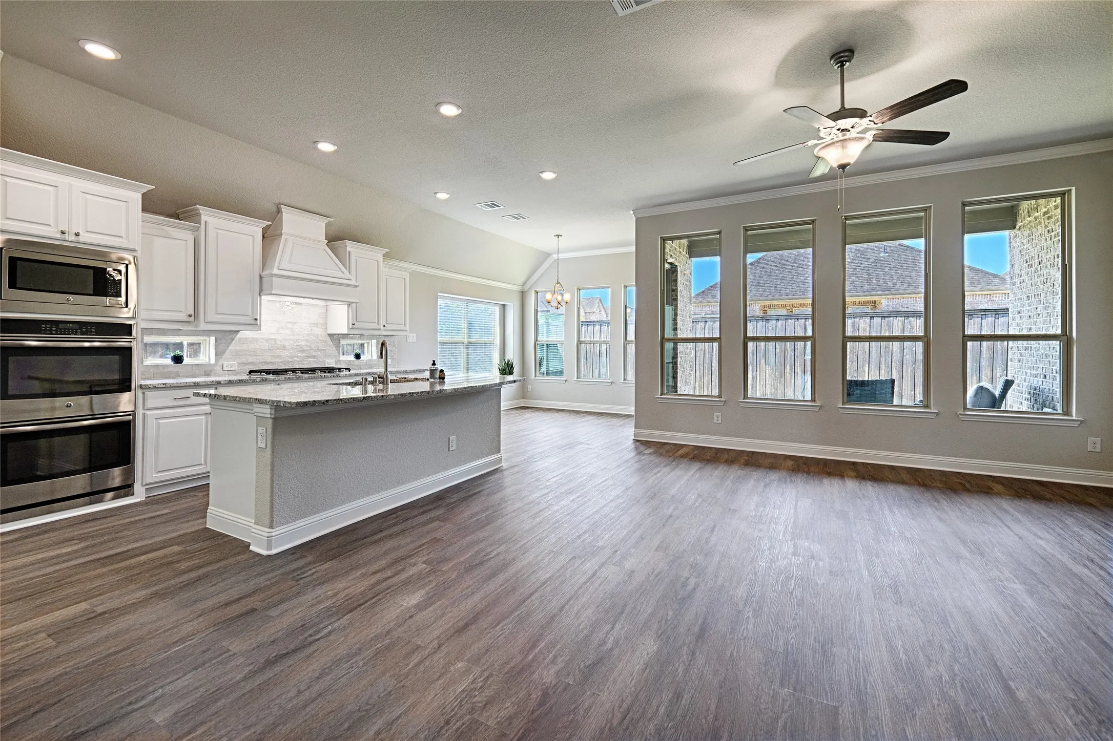 Open-concept floorplan featuring wood-finish flooring, a kitchen island with granite countertop, stainless steel appliances, and a vaulted ceiling