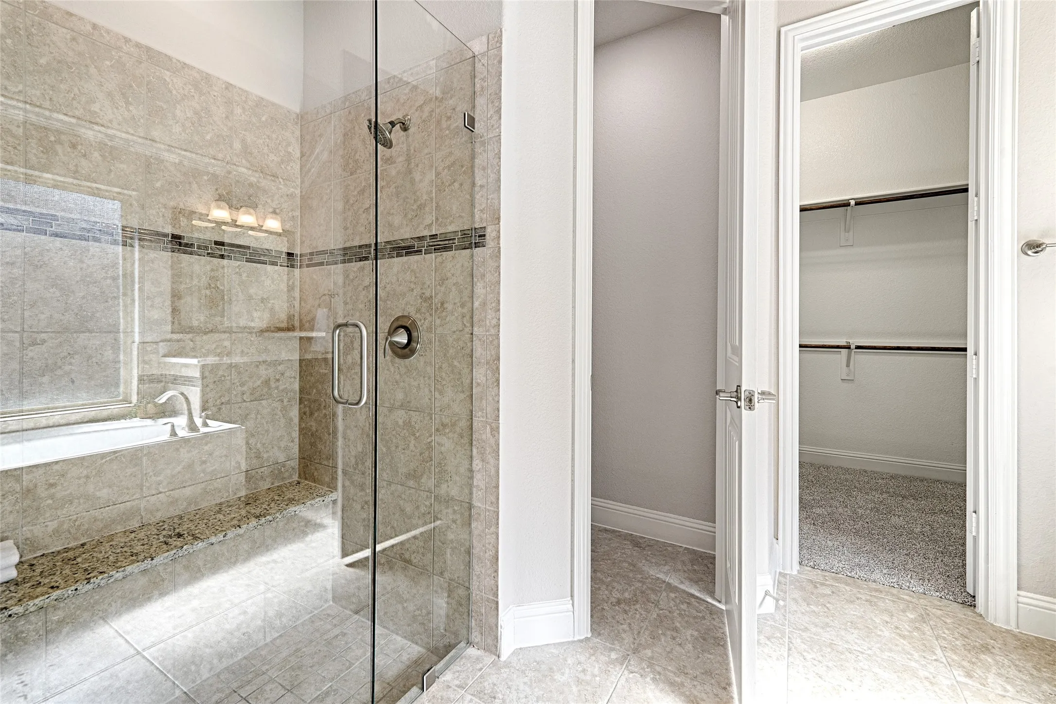 Glass-enclosed shower with tiled walls and integrated bench, separate soaking tub with deck, and overhead light fixture