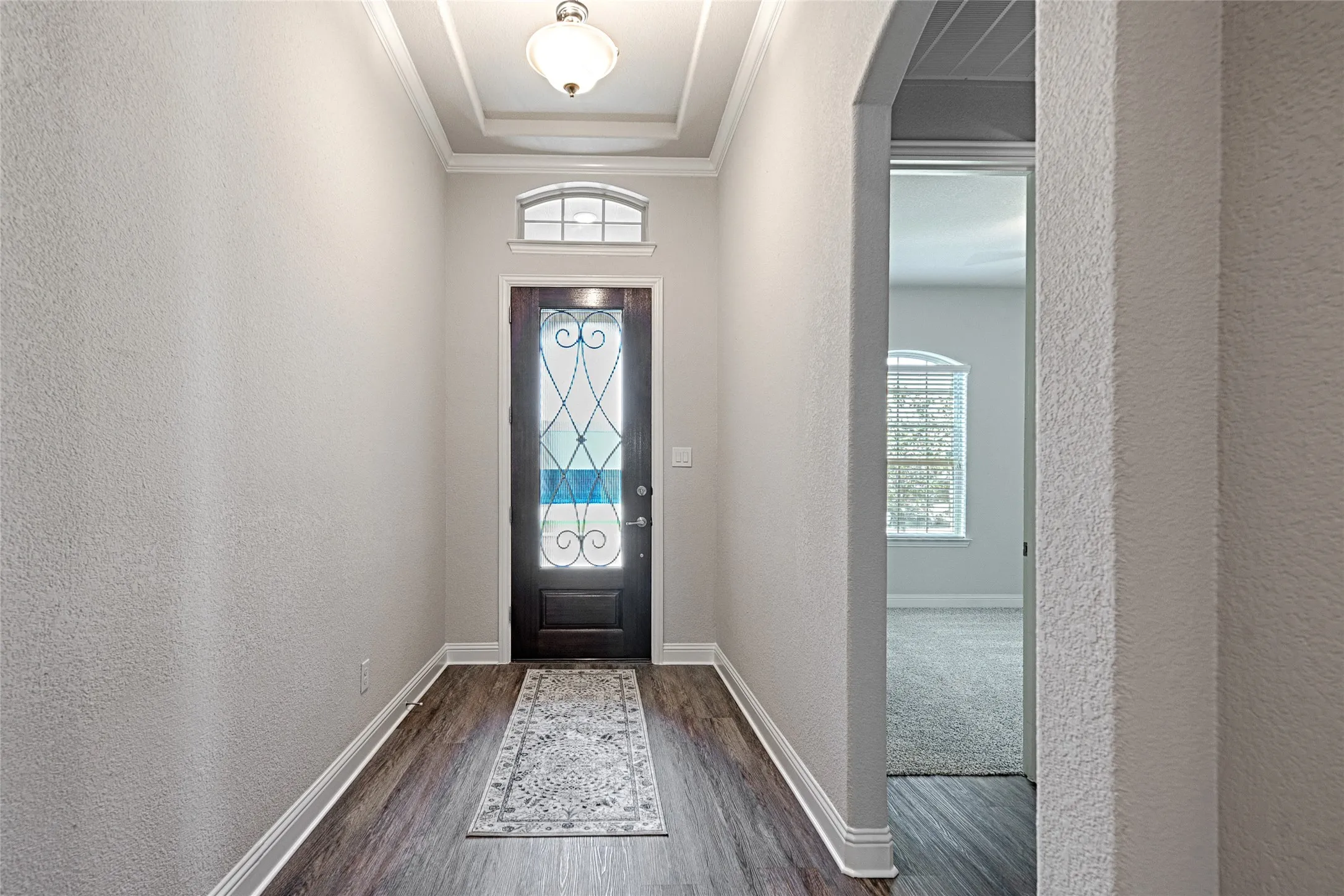 Entryway featuring a dark wood door with decorative glass, an arched transom window, wood-finish flooring and a tray ceiling