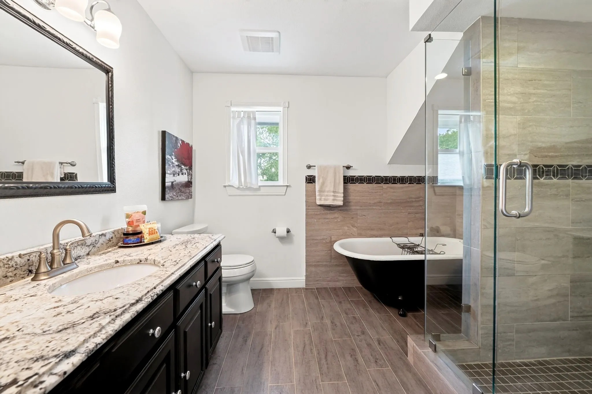 Granite countertop vanity with undermount sink, wood-finish flooring, freestanding soaking tub, and glass-enclosed shower