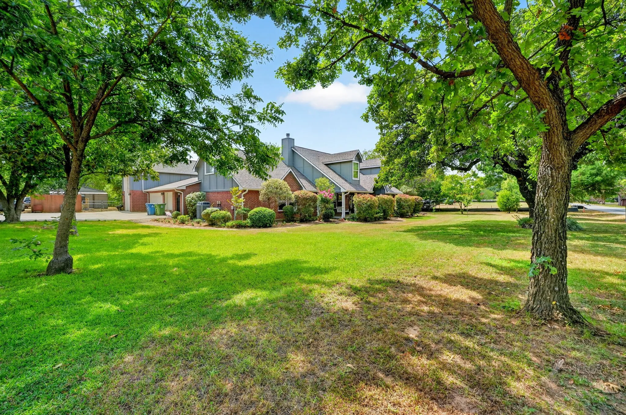 Expansive lawn with mature trees, brick and siding exterior, and a gabled roofline