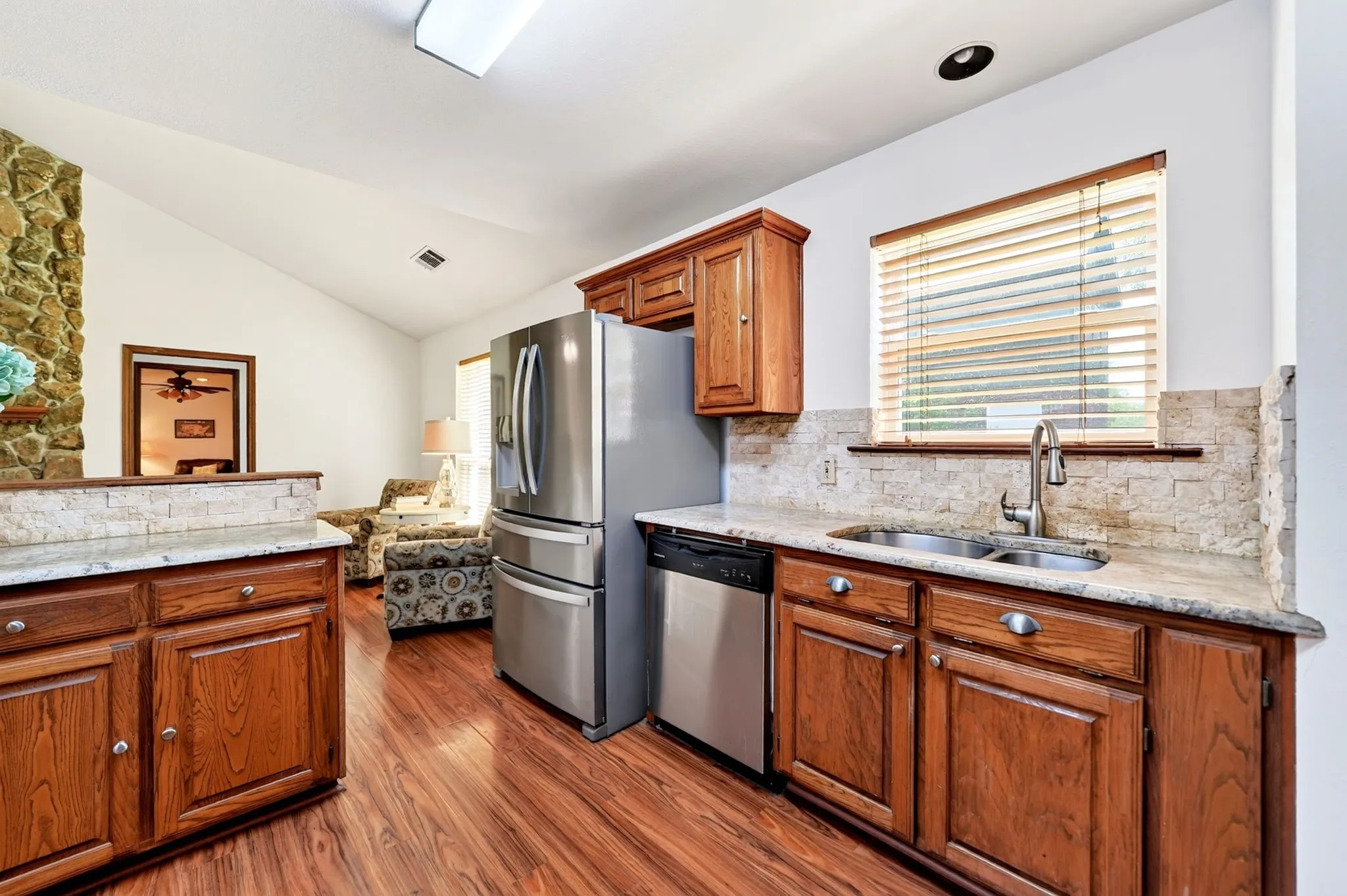 Kitchen featuring wood-finish flooring, wood cabinetry, stone countertops, stainless steel appliances, and a stone backsplash