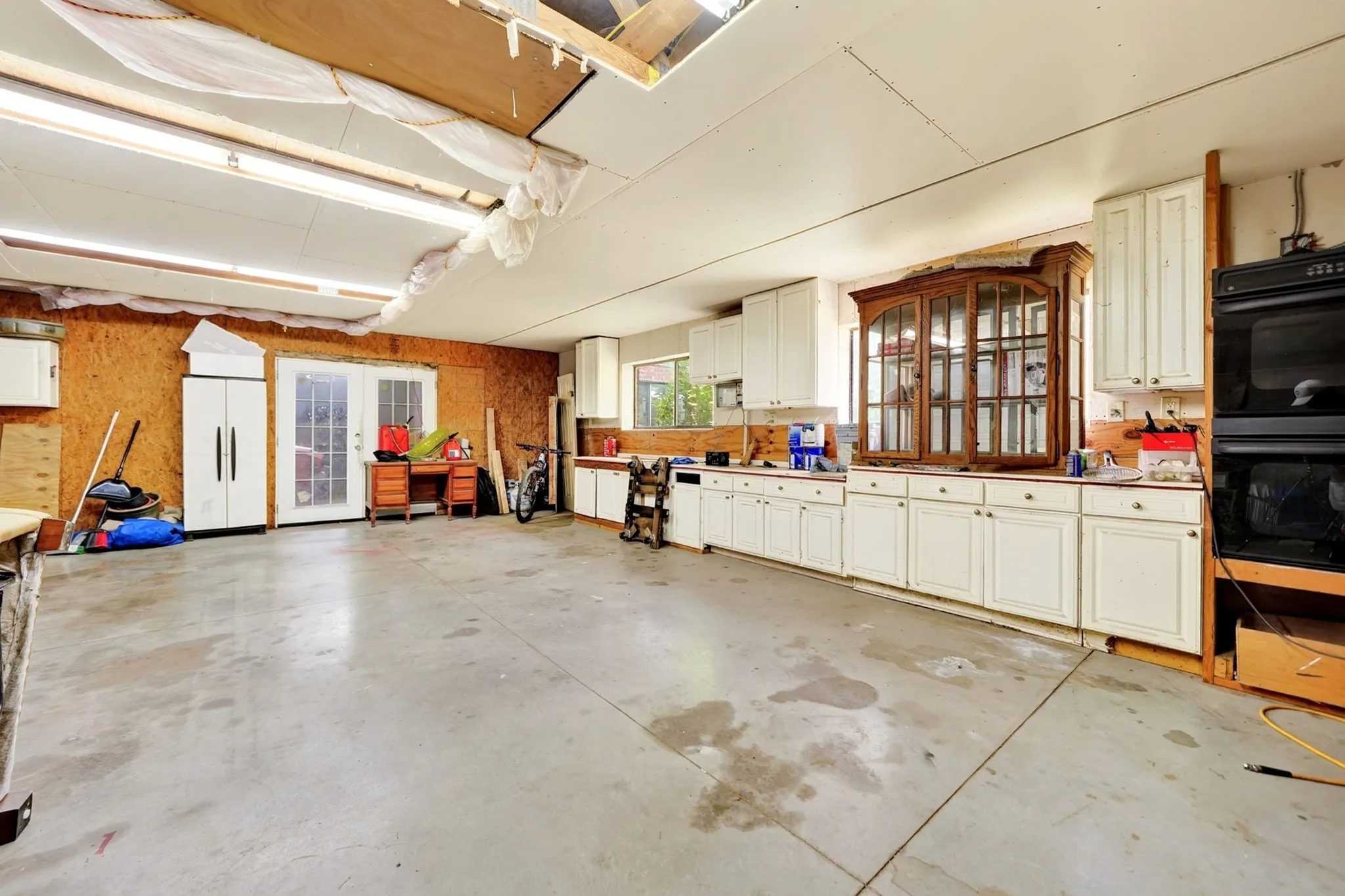 Concrete flooring with extensive white cabinetry, built-in double ovens, and a pair of French doors
